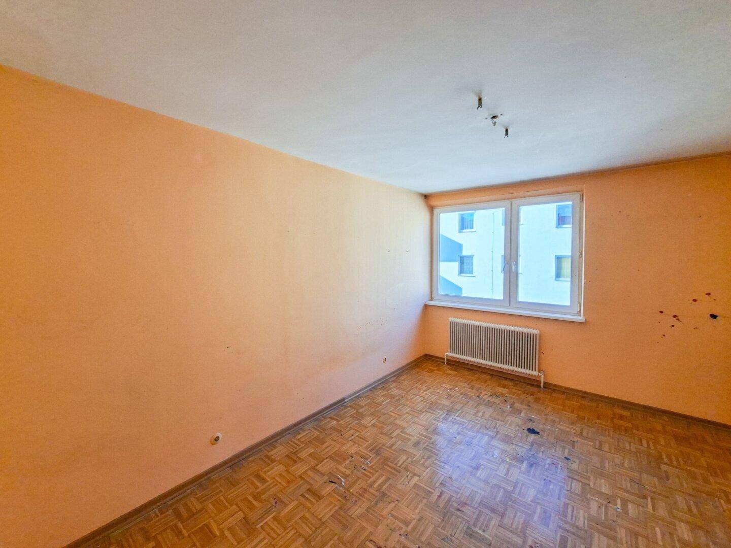 Zimmer mit Fischgrätparkett, pfirsichfarbenen Wänden und einem Fenster mit Blick nach draußen.