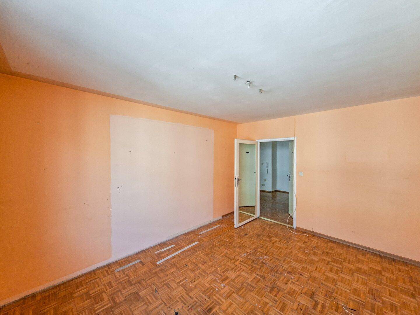 Leeres Zimmer mit Fischgrätparkett und pfirsichfarbenen Wänden, ideal für eine Renovierung.