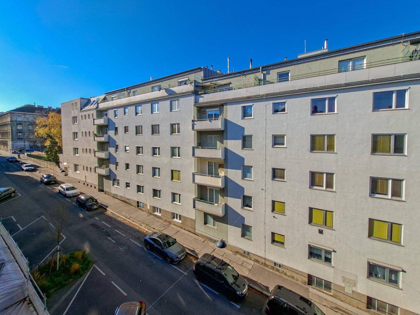 Ansicht eines Mehrfamilienhauses entlang einer Straße mit geparkten Autos.
