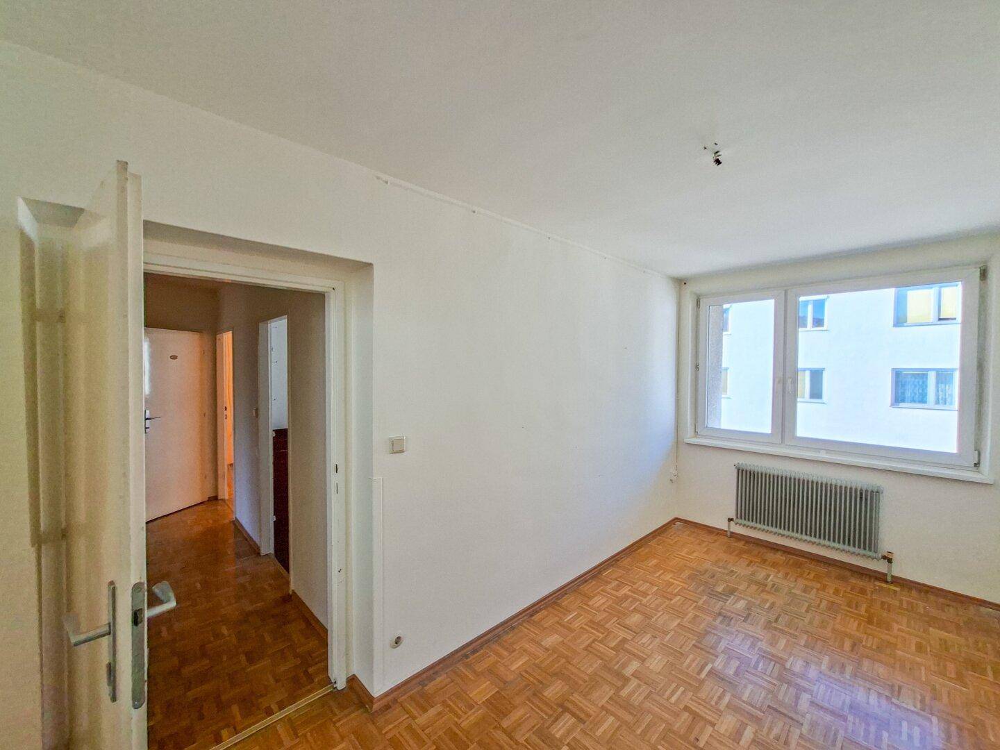 Helles Zimmer mit Fischgrätparkett, weißen Wänden und einem Fenster.