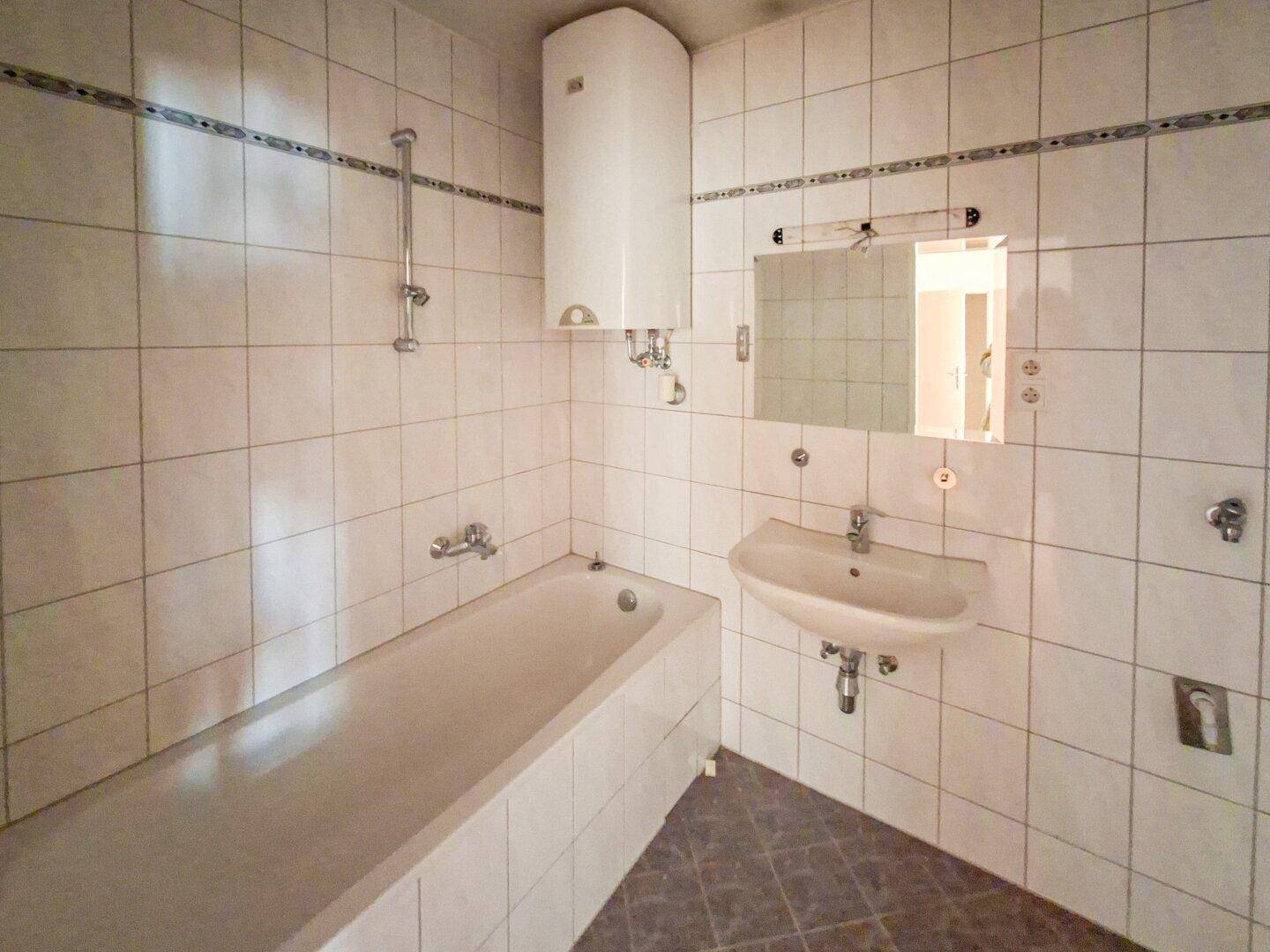 Badezimmer mit weißen Fliesen, einer Badewanne und einem einzelnen Waschbecken.