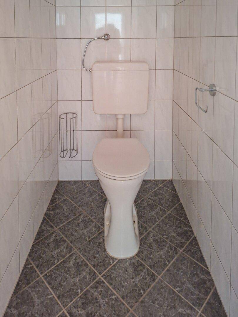 Separates WC mit weißen Wandfliesen und grauen Bodenfliesen.