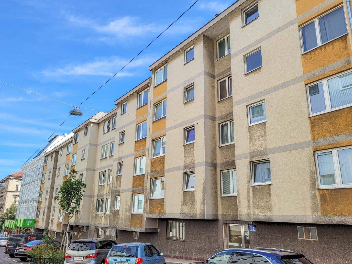 Fassade eines Wohngebäudes entlang einer Straße mit geparkten Fahrzeugen.