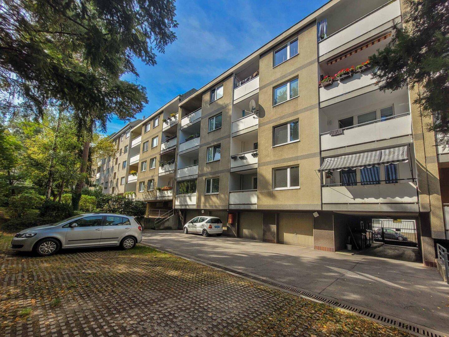 Wohngebäude mit Balkonen und umgebenden Grünflächen unter blauem Himmel.