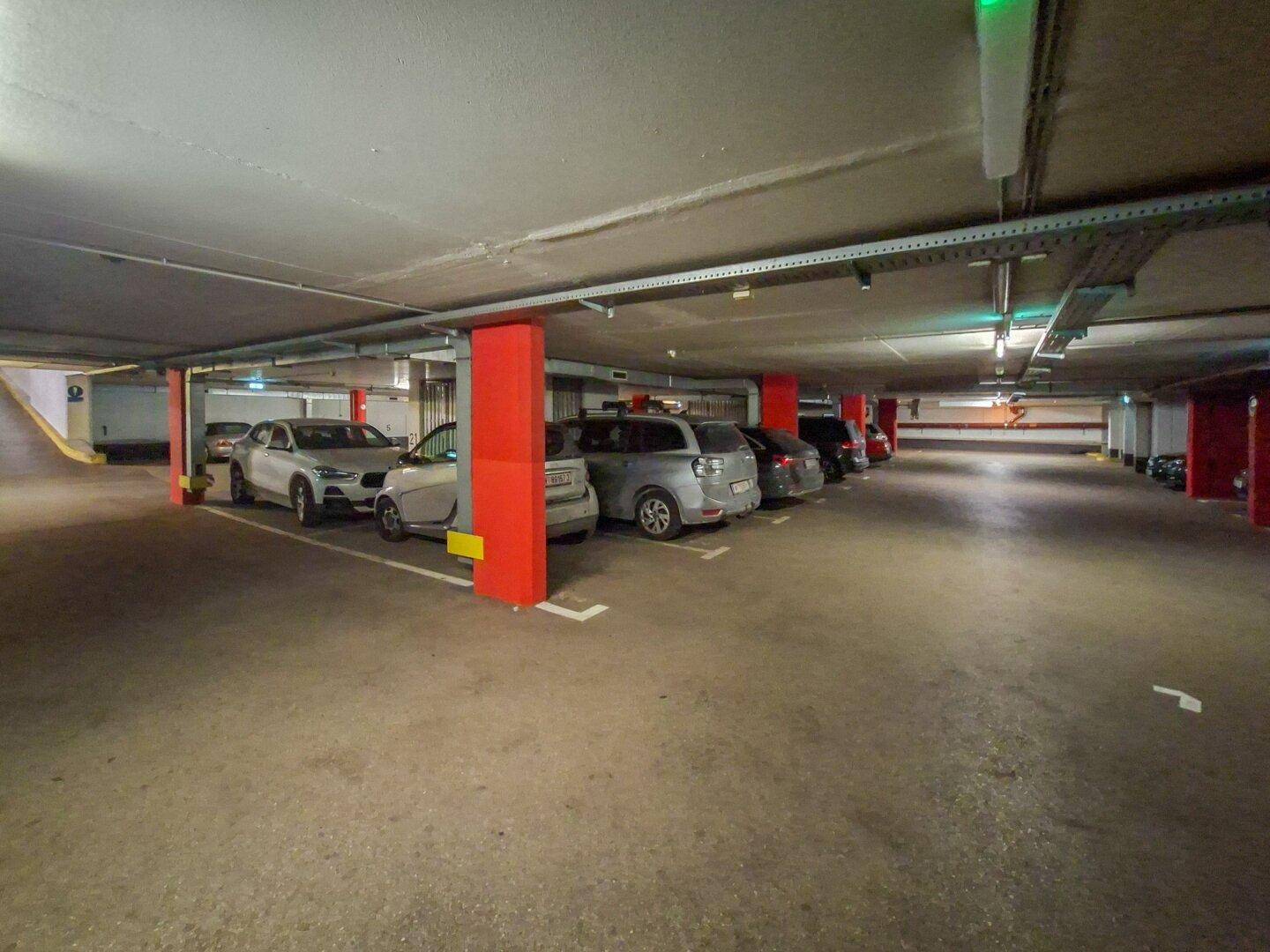 Weitere Ansicht der Tiefgarage mit vielen Stellplätzen und roten Stützpfeilern.