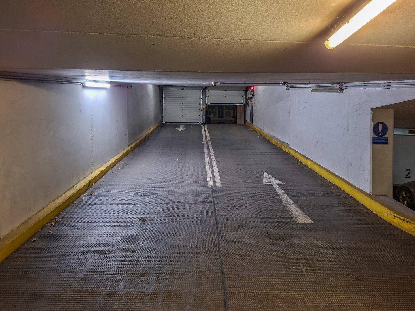 Zufahrtsrampe zur Tiefgarage mit doppelter Fahrspur und klaren Richtungspfeilen.
