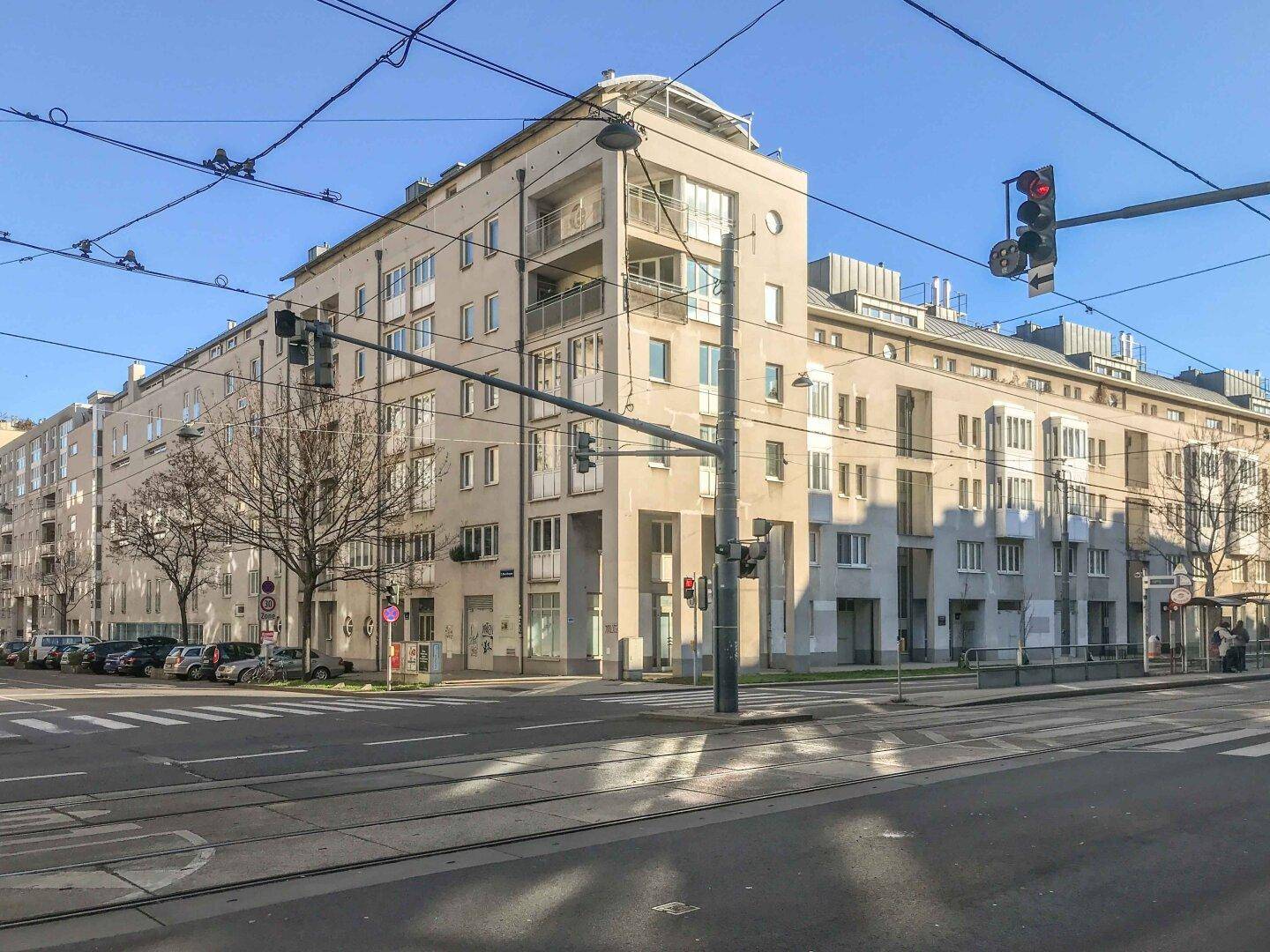 Modernes Wohngebäude an einer belebten Straße mit Straßenbahnschienen und Ampeln.