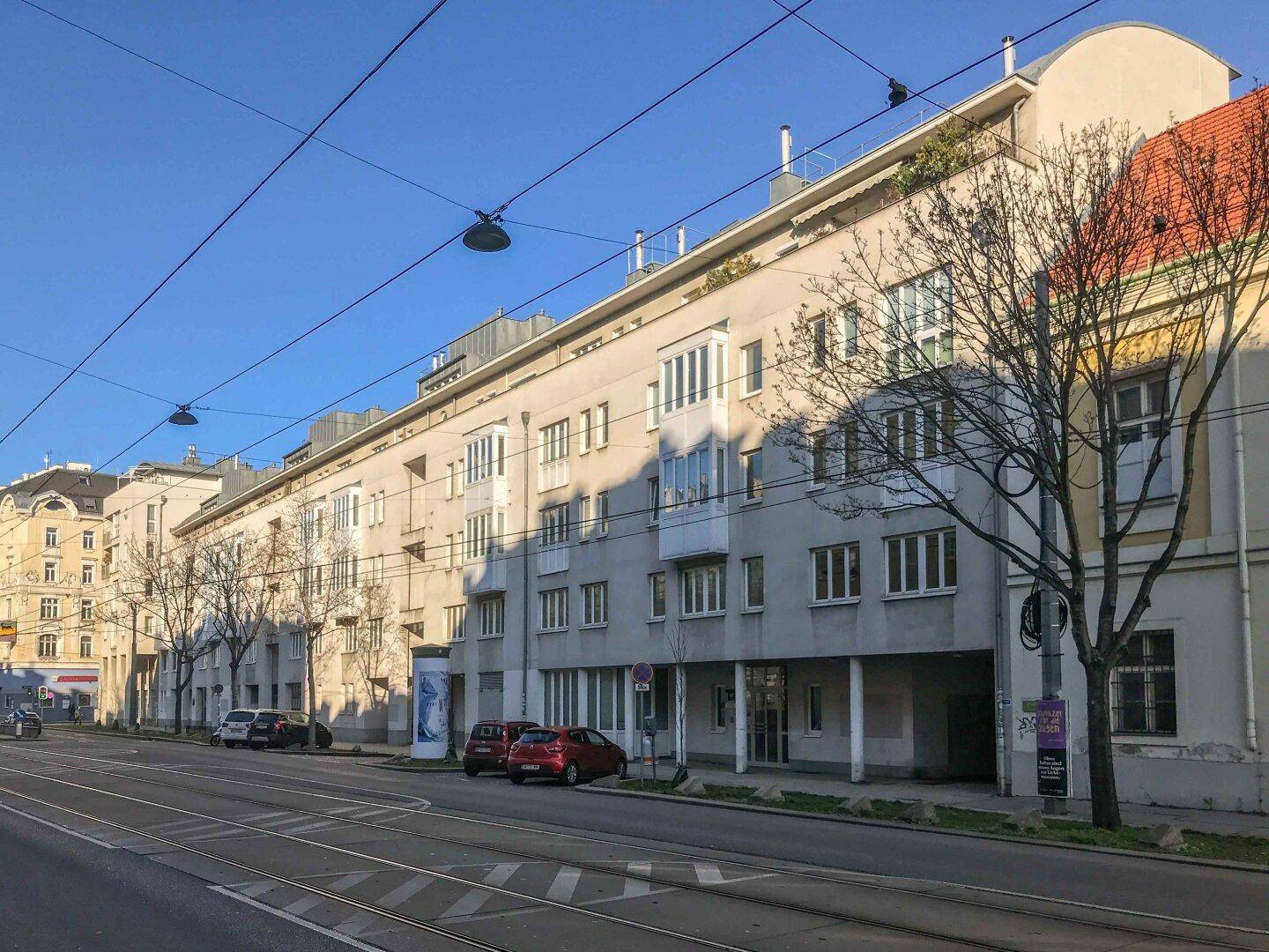 Lange Fassade eines Wohnkomplexes entlang einer städtischen Straße mit Bäumen.
