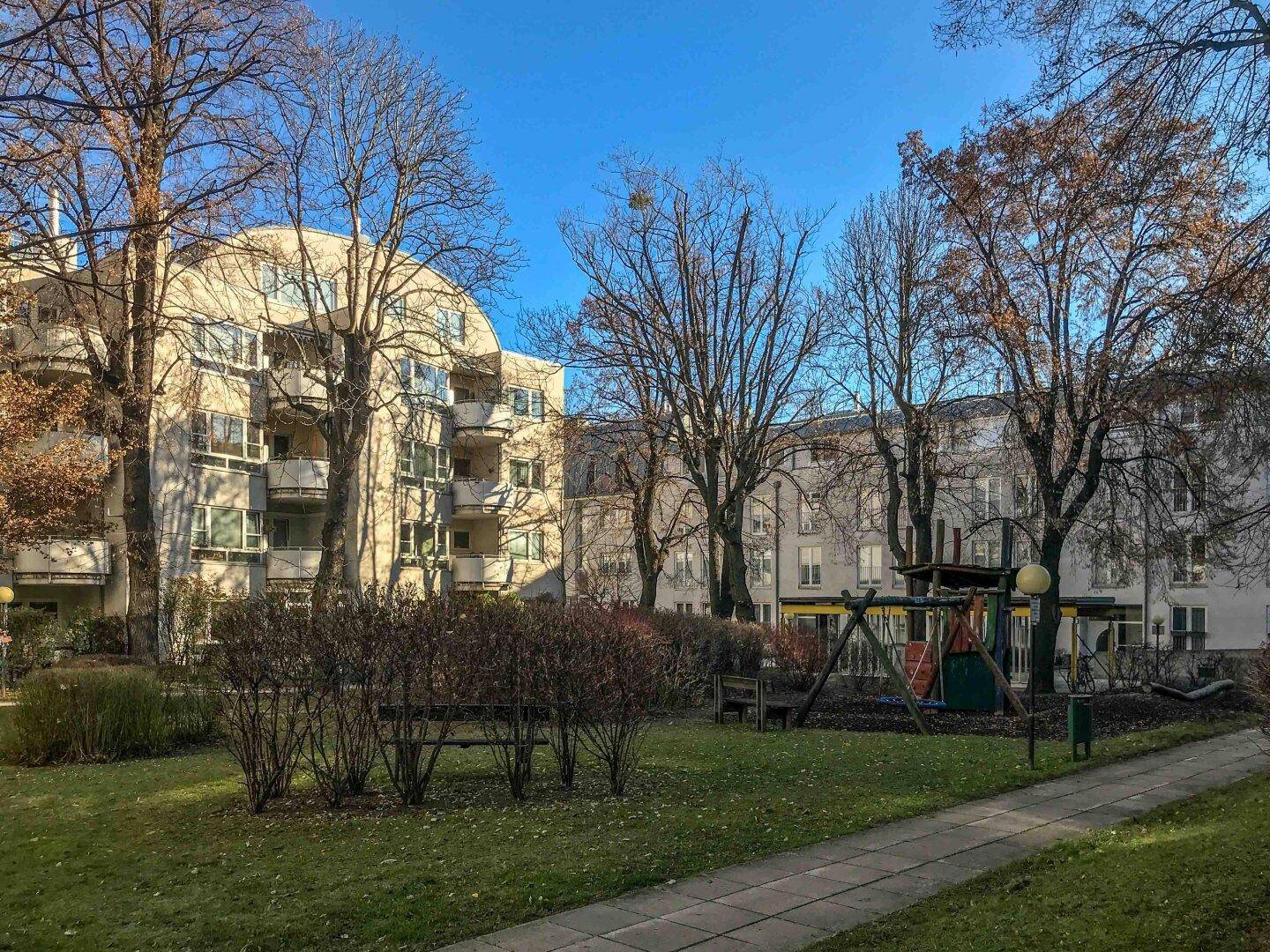 Grüner Innenhof mit Spielplatz und hohen Bäumen, umgeben von Wohngebäuden.