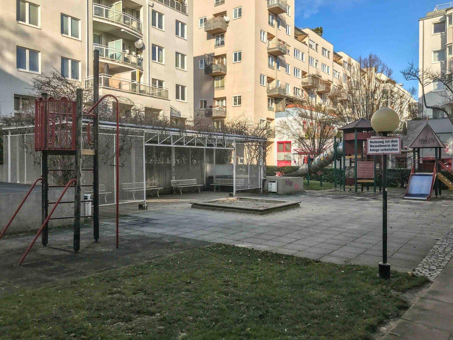 Großer Spielplatz im Innenhof mit Sandkasten, Rutschen und Klettergeräten.