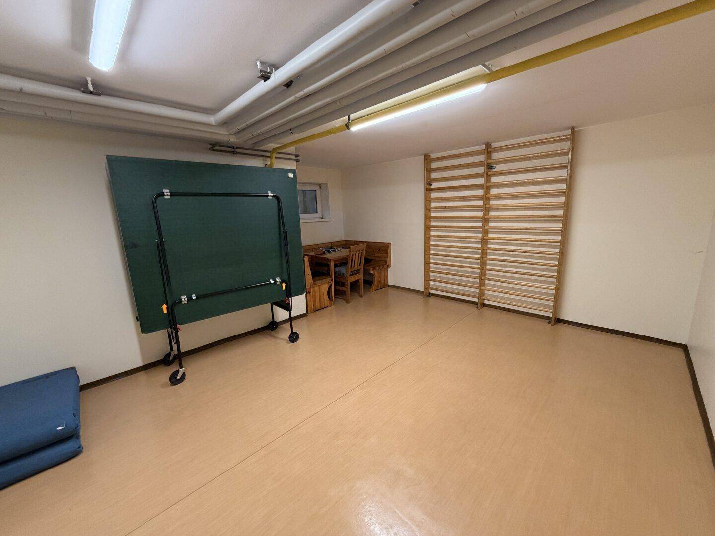 Freizeitraum im Keller mit Tischtennisplatte und Sprossenwand für sportliche Aktivitäten.