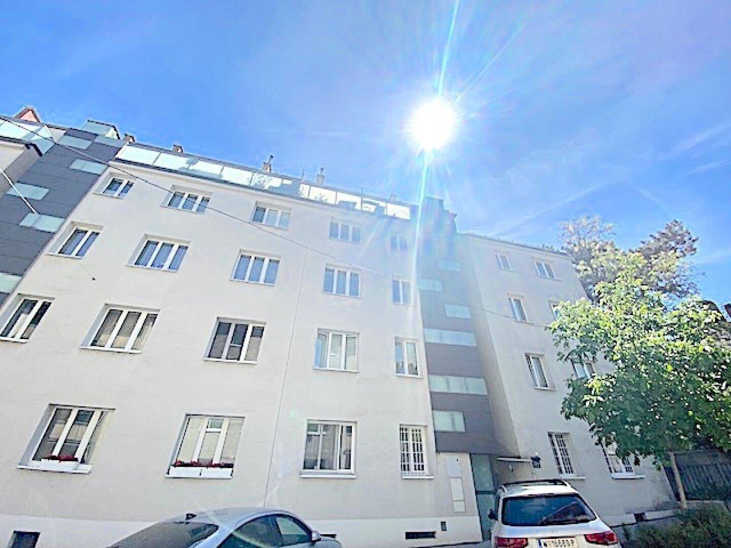 Mehrstöckiges Wohngebäude mit heller Fassade und vielen Fenstern unter blauem Himmel.