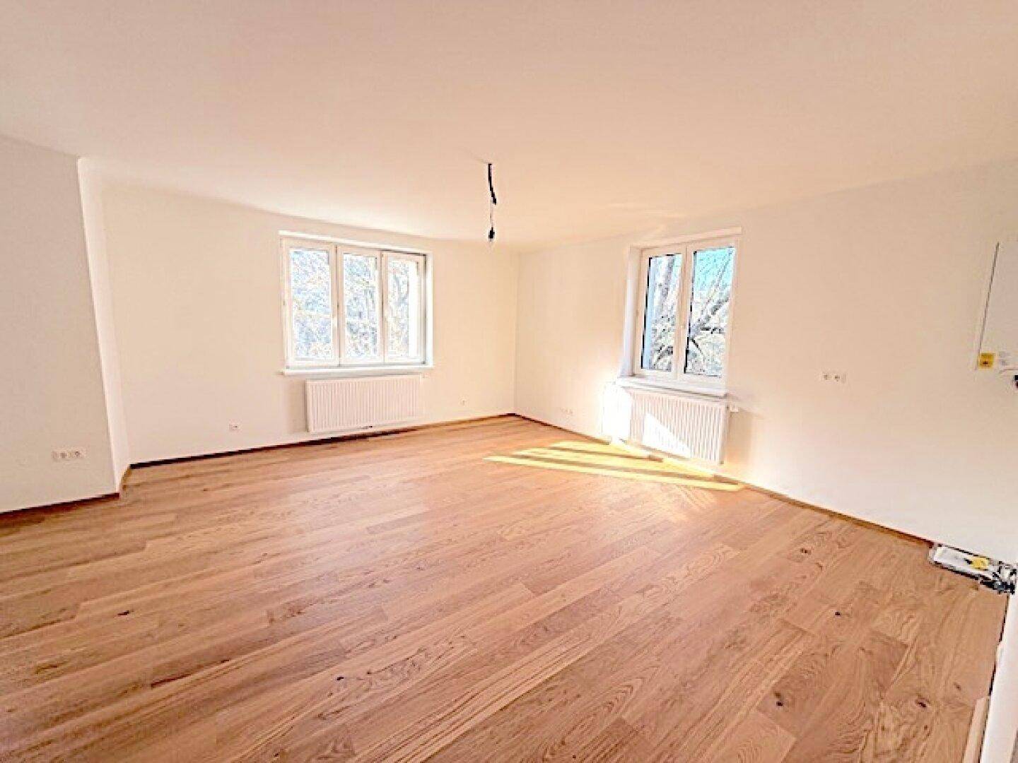 Helles und geräumiges Zimmer mit Holzboden und großen Fenstern, ideal für Wohnzwecke.