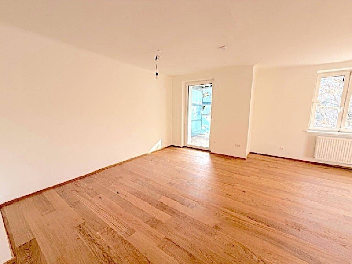 Helles Zimmer mit Holzboden und Zugang zu einem Balkon, ideal für einen Wohnbereich.