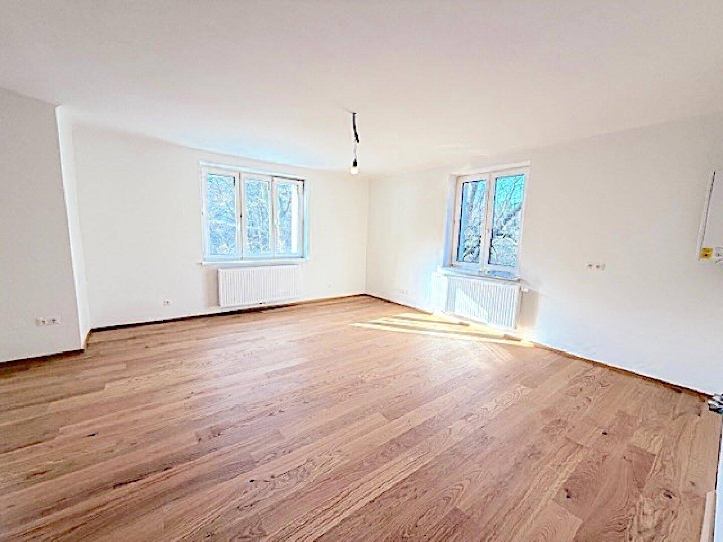 Helles und geräumiges Zimmer mit Holzboden und großen Fenstern, ideal für Wohnzwecke.