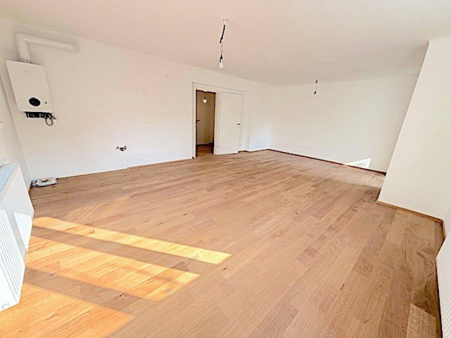 Leerer Raum mit Holzboden und weiß gestrichenen Wänden, inklusive Heizungsanlage.