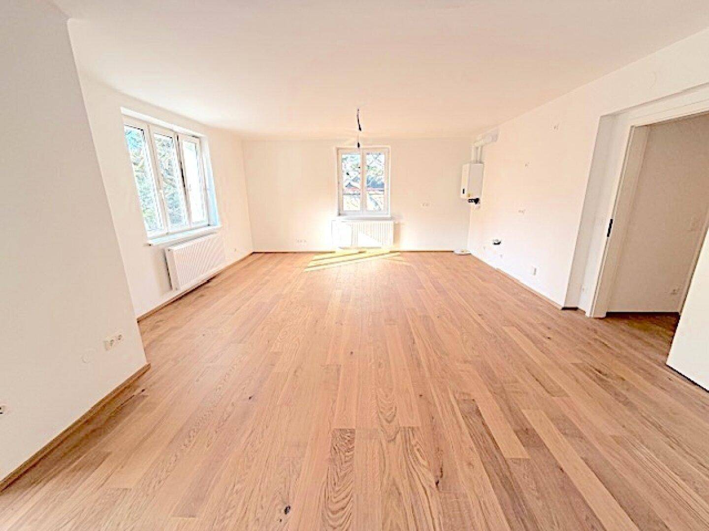 Geräumiges, leeres Zimmer mit hellem Holzboden und großen Fenstern, bereit zur Einrichtung.