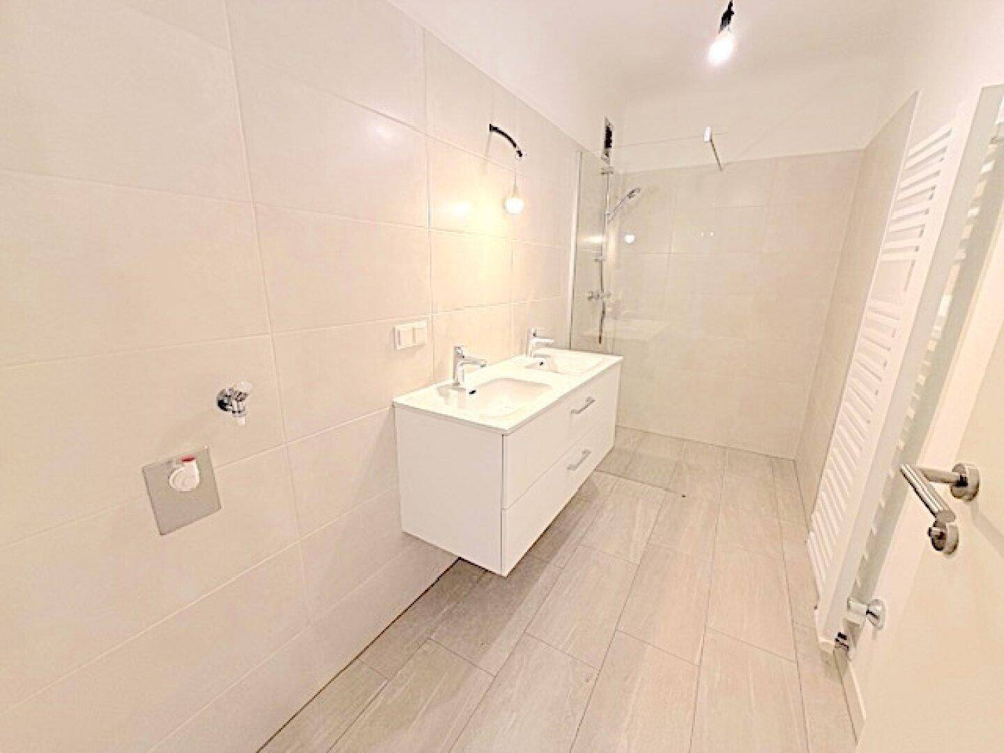 Modernes Badezimmer mit hellen Fliesen, Doppelwaschbecken und begehbarer Dusche.