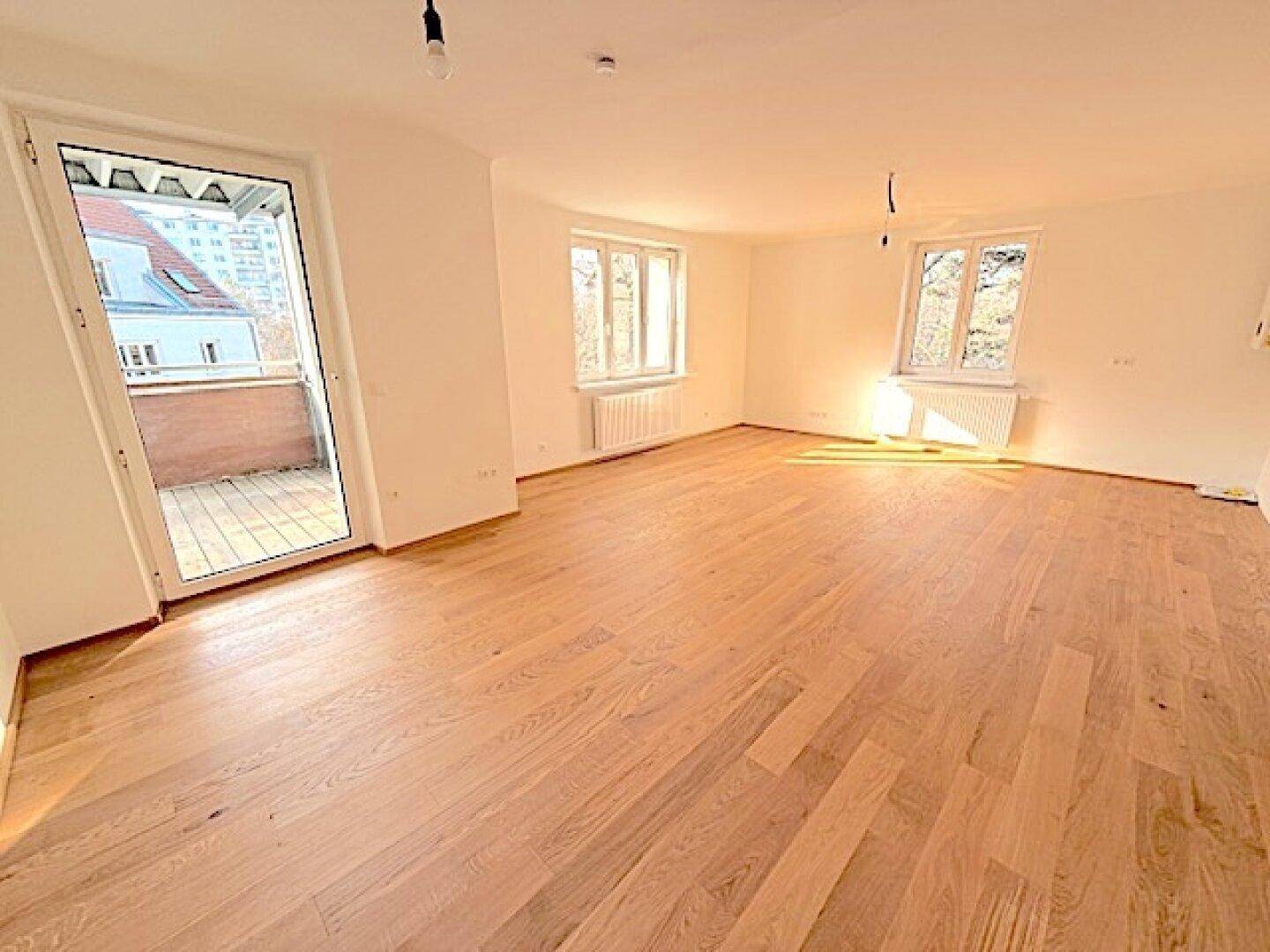 Helles Zimmer mit Holzboden und Zugang zu einem Balkon, ideal für einen Wohnbereich.
