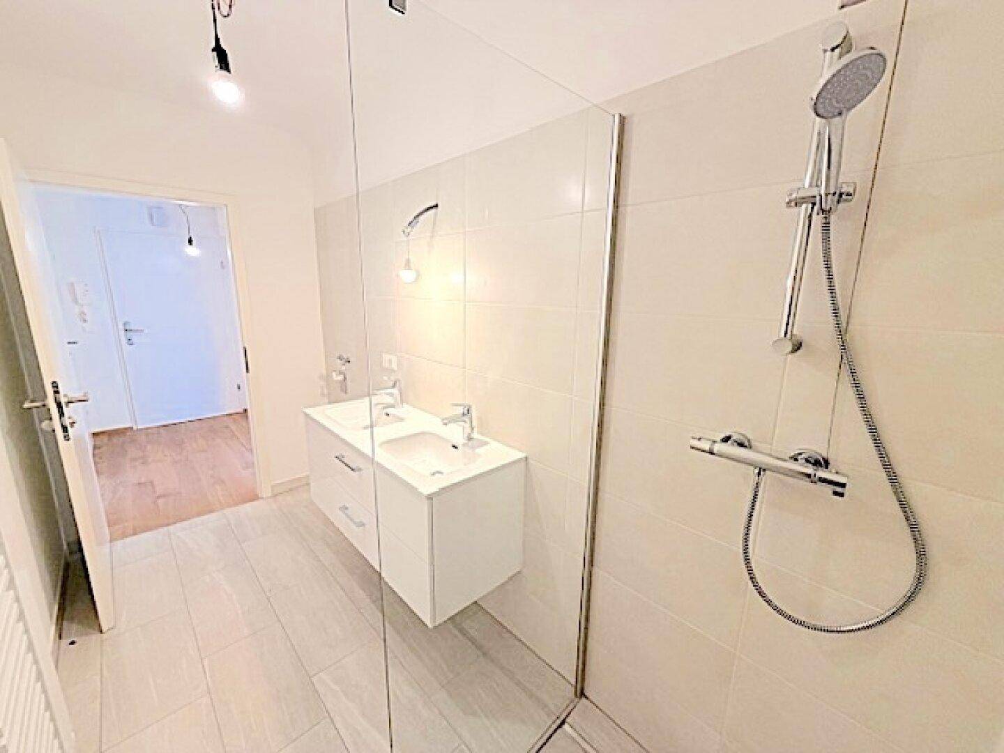 Modernes Badezimmer mit hellen Fliesen, Doppelwaschbecken und begehbarer Dusche.