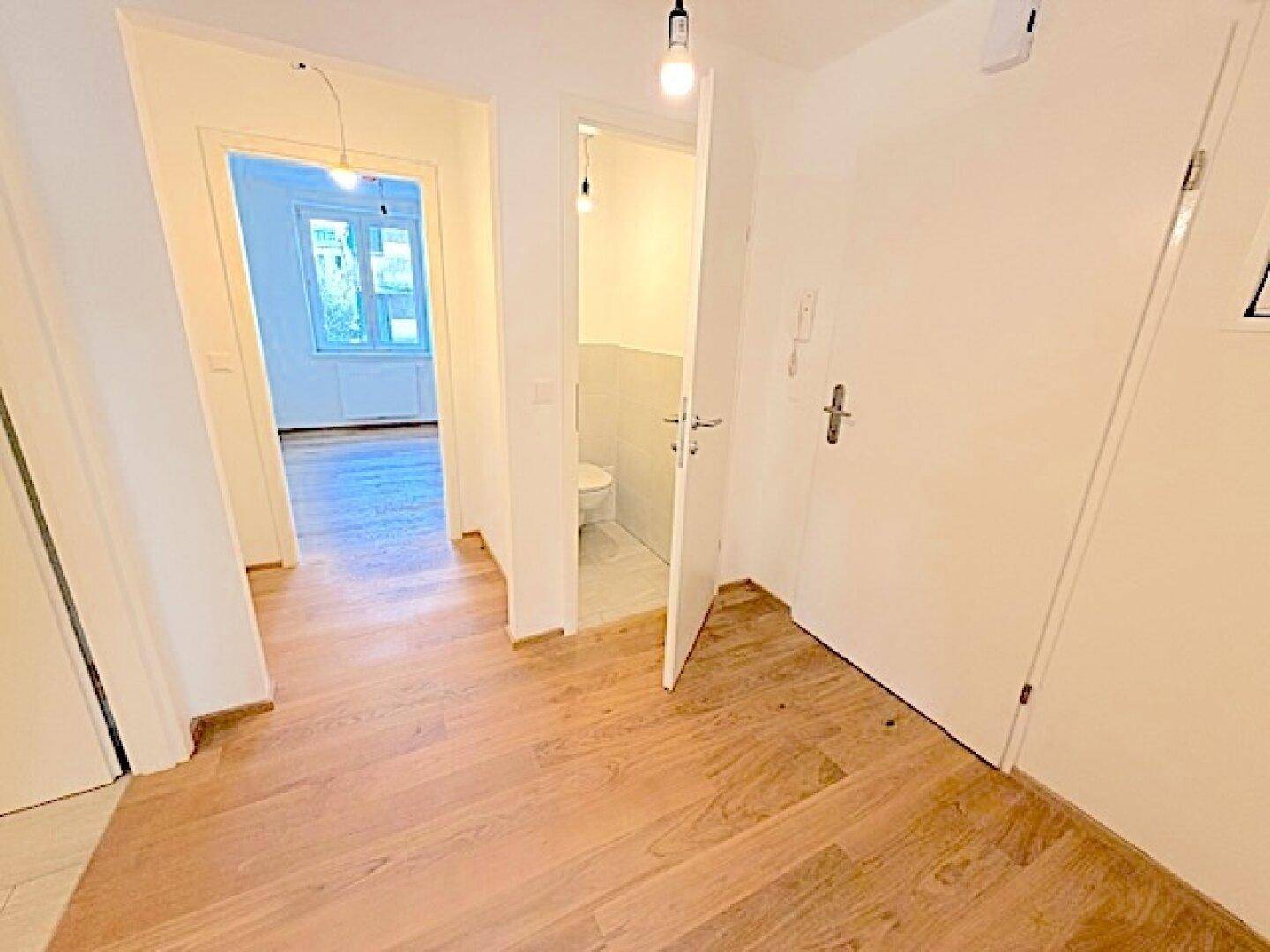 Flur mit Holzparkettboden und Zugang zu einem Gäste-WC sowie weiteren Zimmern.