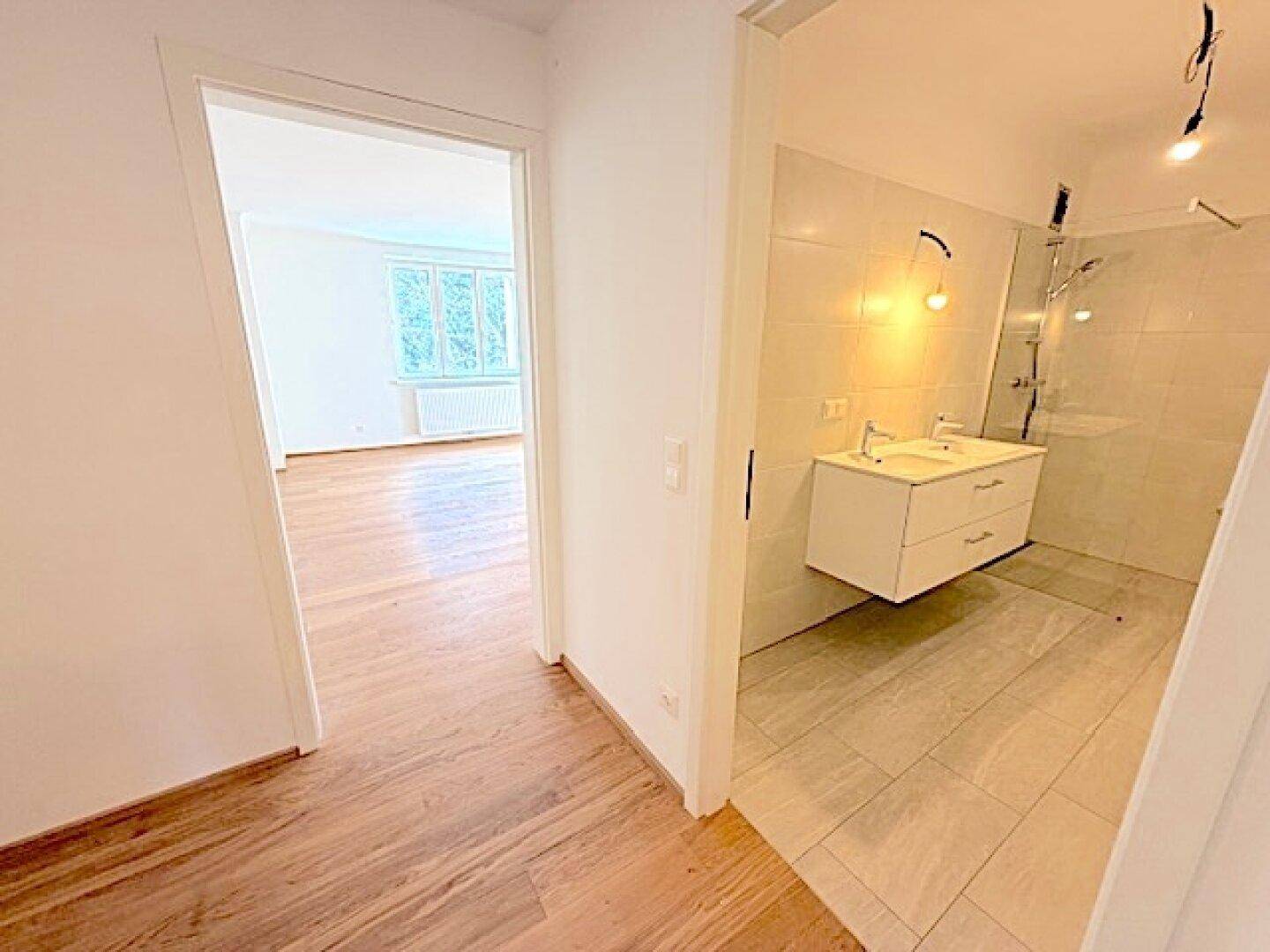Flur mit Holzparkettboden und offenem Blick in ein modernes Badezimmer mit Doppelwaschbecken.