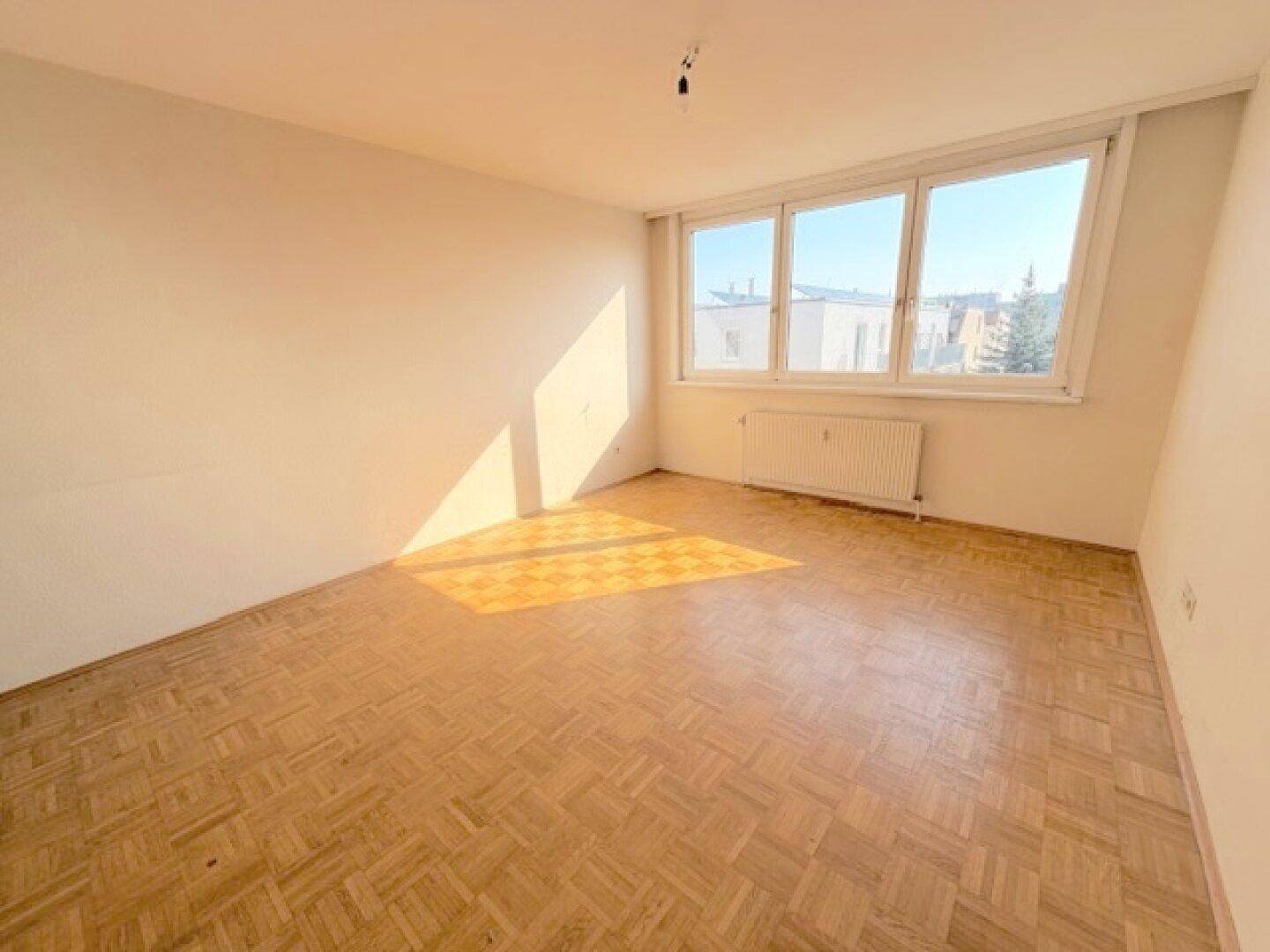 Helles, leeres Zimmer mit Parkettboden und weitem Blick durch die großen Fenster.