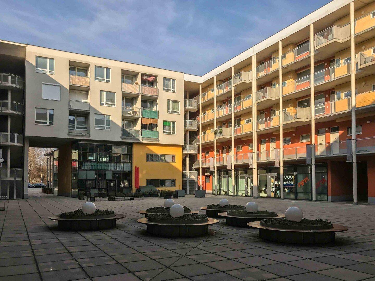 Heller Innenhof mit modernen Wohngebäuden, bunten Balkonen und Sitzgelegenheiten.