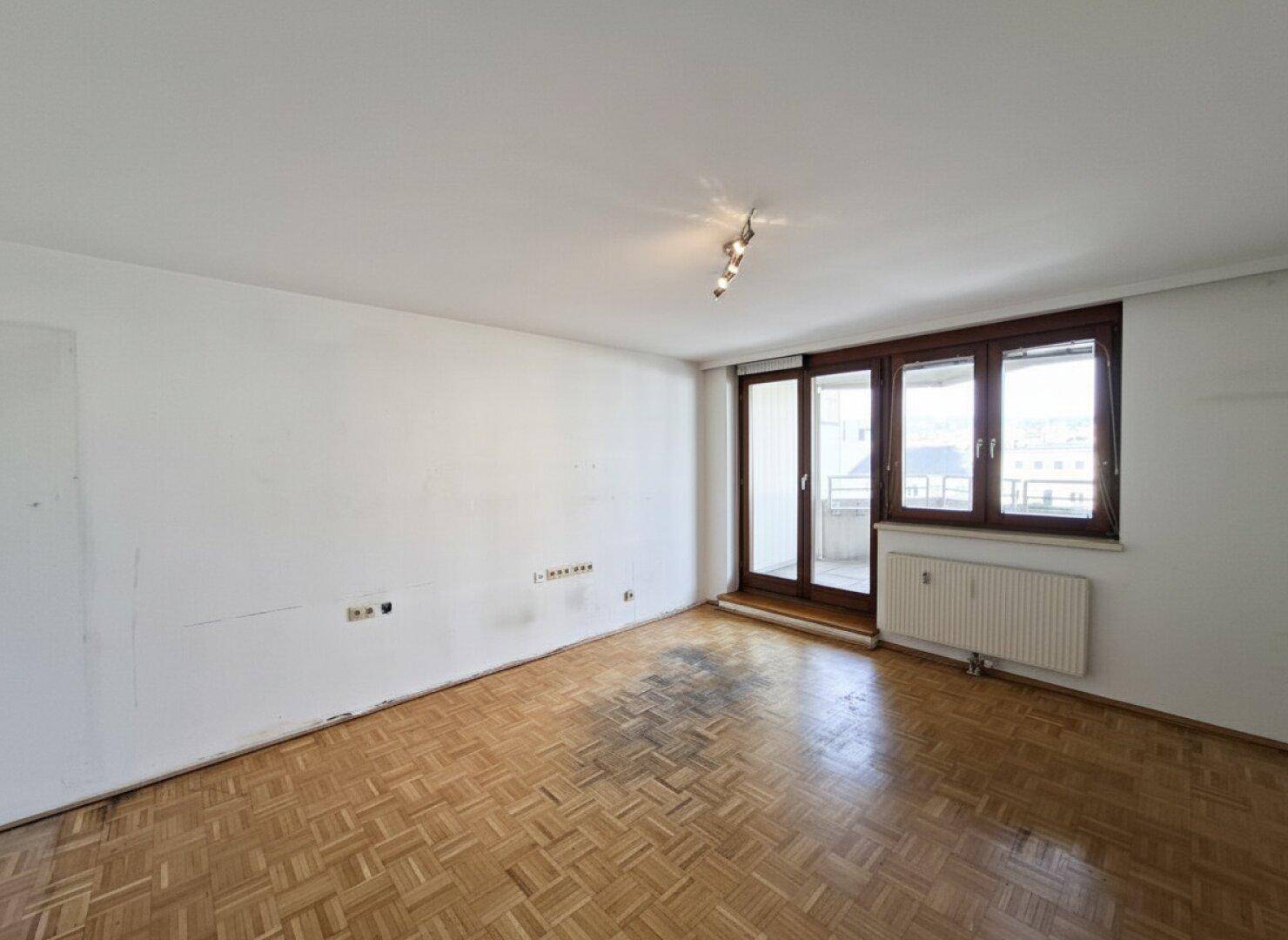 Leeres Wohnzimmer mit Parkettboden und Zugang zum Balkon, bereit zur individuellen Gestaltung.