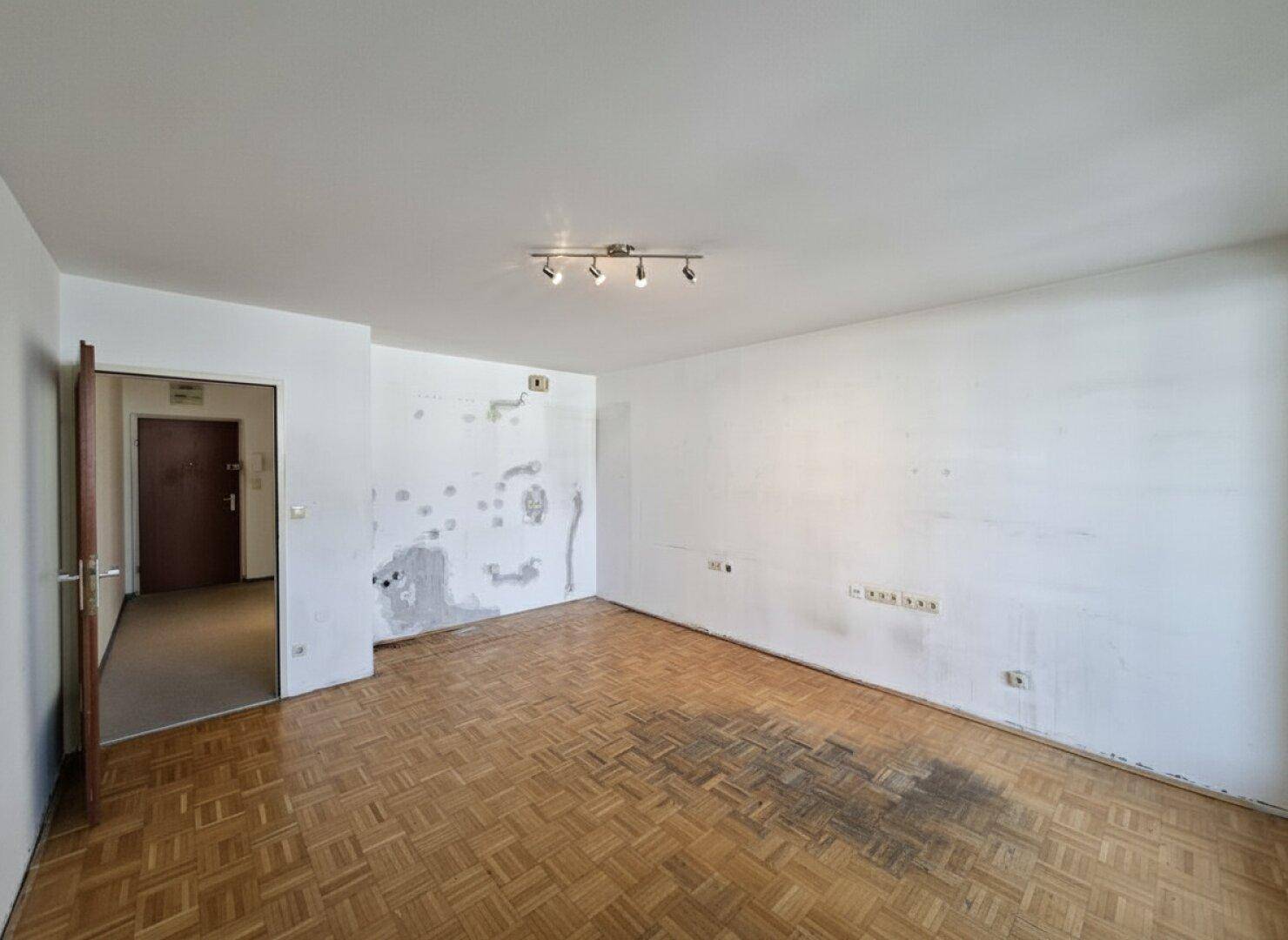 Geräumiges Wohnzimmer mit Parkettboden und Spuren früherer Wandgestaltung, ideal für Renovierung.