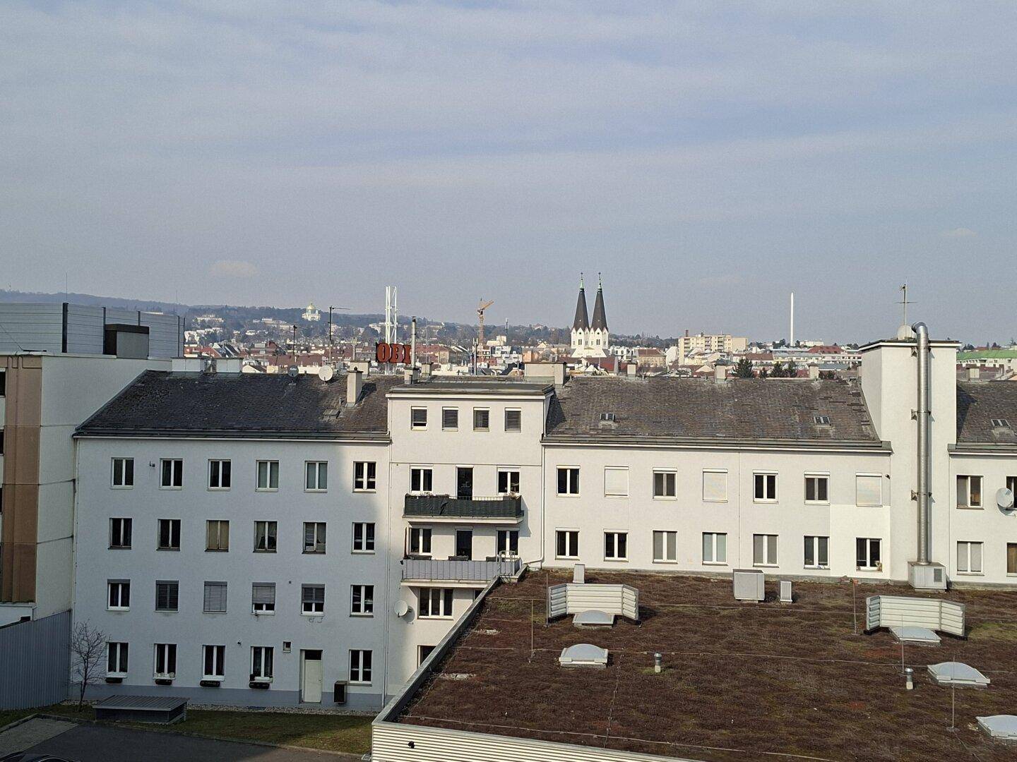 Weitläufiger Stadtblick mit Kirchtürmen und umliegenden Gebäuden unter blauem Himmel.