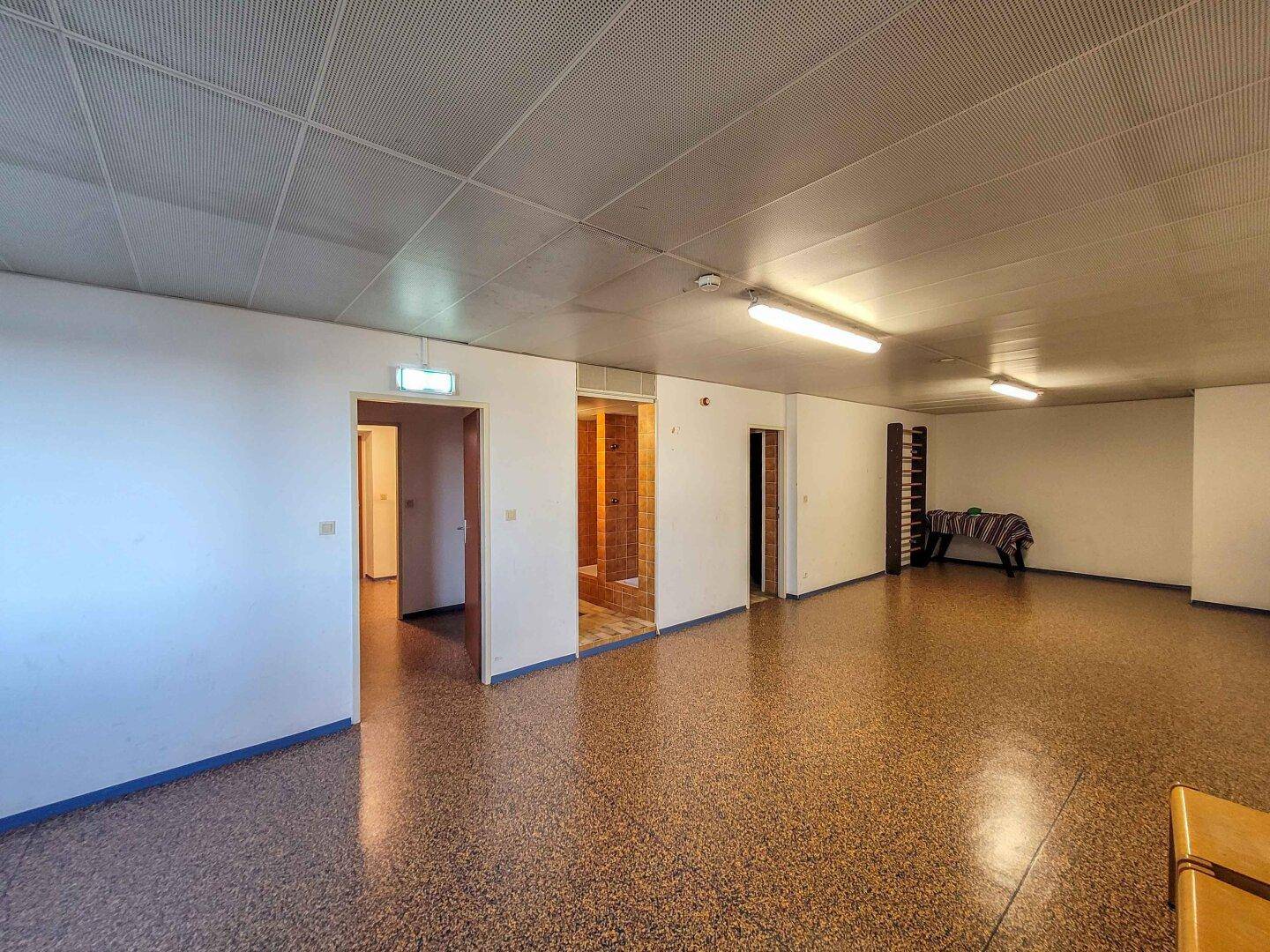 Großer Gemeinschaftsraum mit Vinylboden und Deckenbeleuchtung, vielseitig nutzbar.