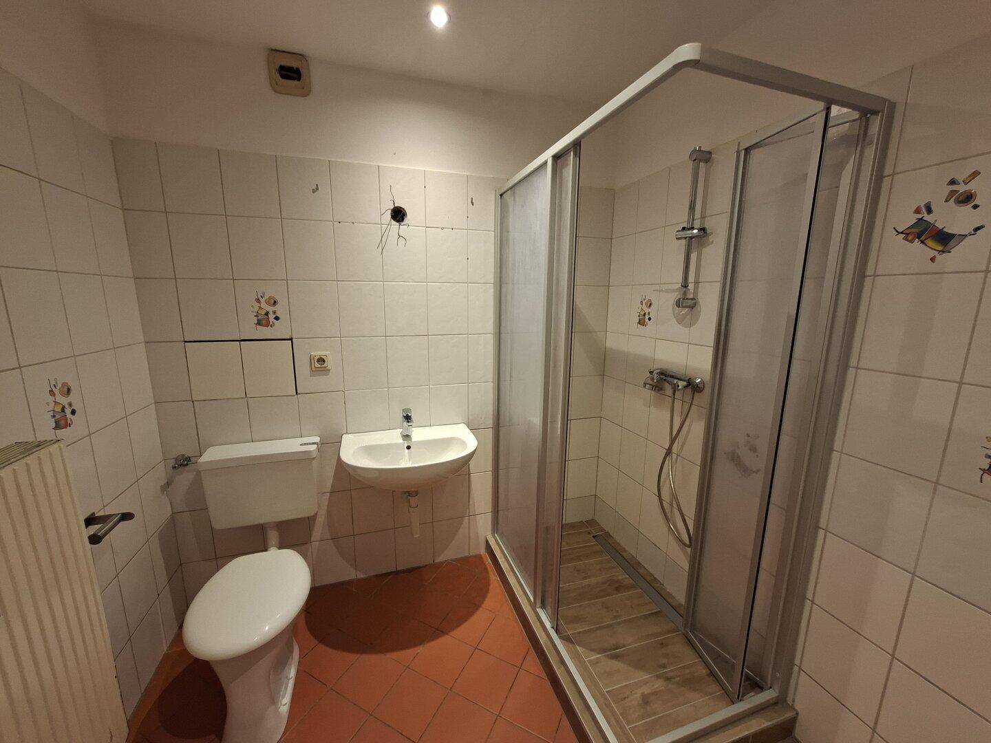 Badezimmer mit Dusche, WC und Waschbecken, ausgestattet mit hellen Fliesen.
