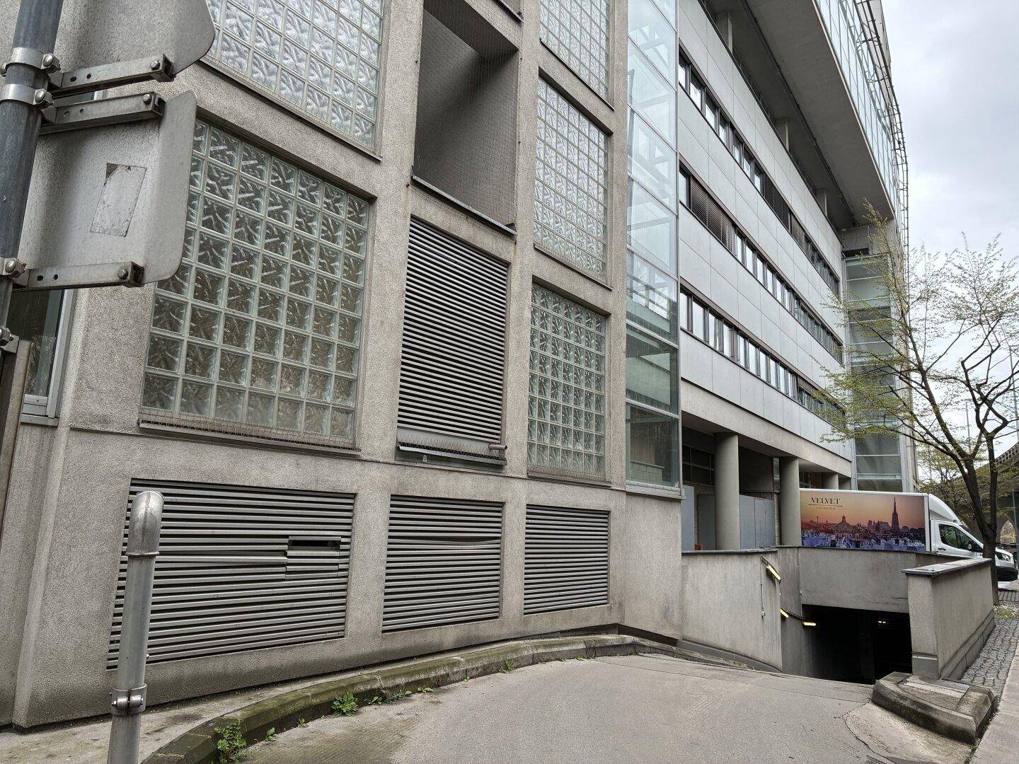 Gebäudeeingang mit Zufahrt zur Tiefgarage und Fassadenelementen aus Glasbausteinen.