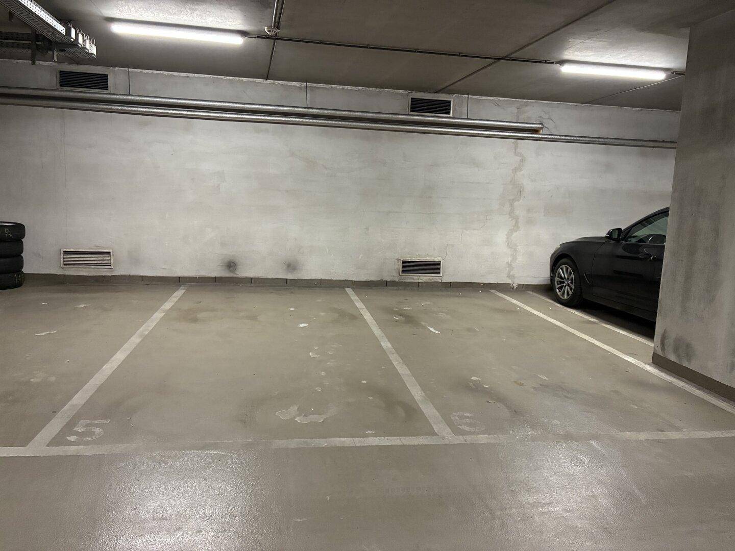 Leerer Stellplatz in der Tiefgarage mit Betonwänden und Deckenbeleuchtung.