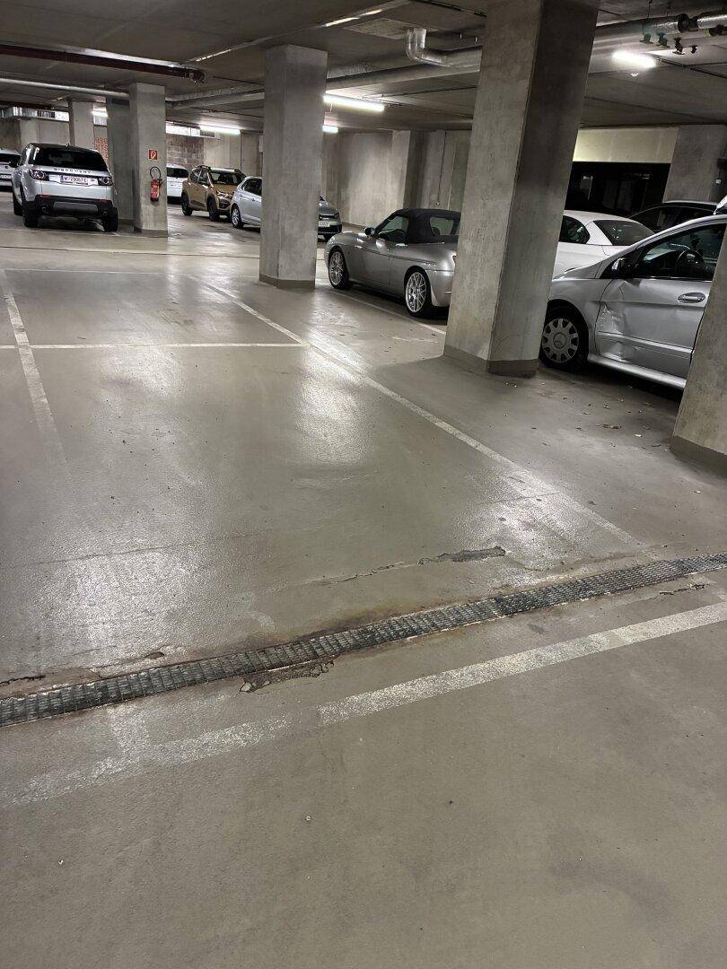 Reihe von Stellplätzen in der Tiefgarage mit Betonpfeilern und Entwässerungsrinne.