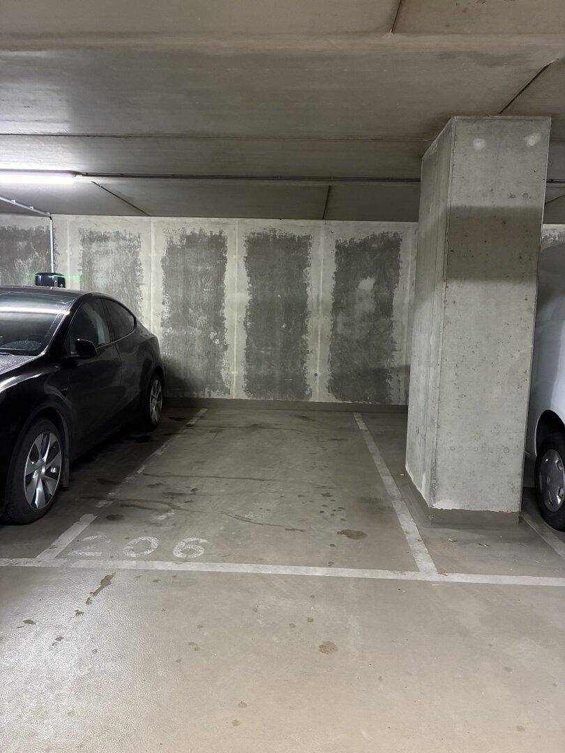Leerer Stellplatz in der Tiefgarage neben einem Betonpfeiler und einer strukturierten Wand.
