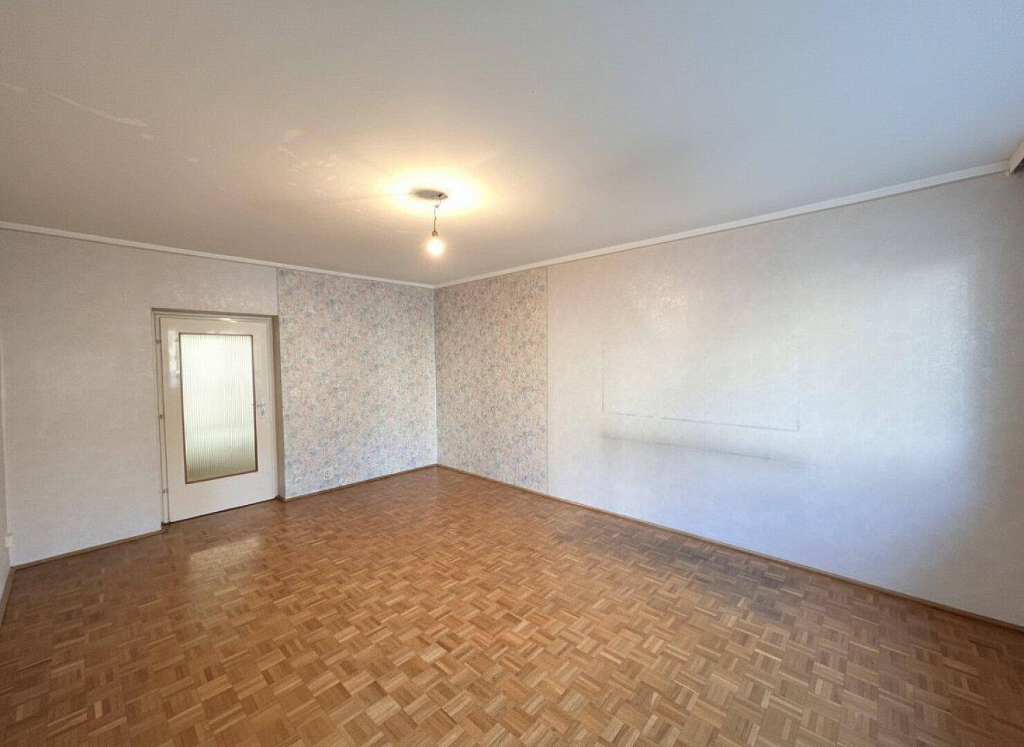 Leerer Raum mit Parkettboden und einer Tür, die zu einem weiteren Bereich führt.