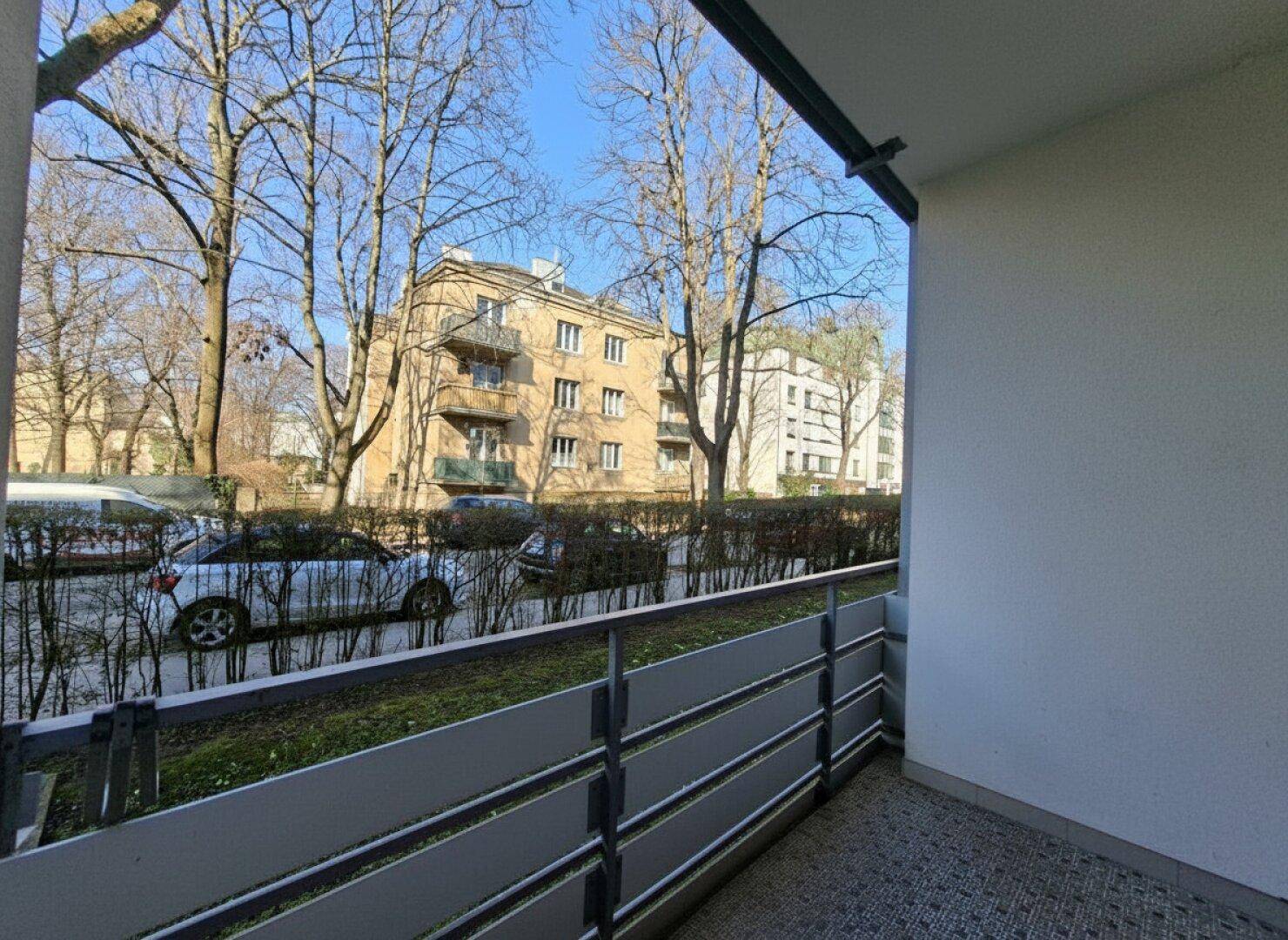 Balkon mit Blick auf die Straße und umliegende Gebäude, umgeben von Bäumen.