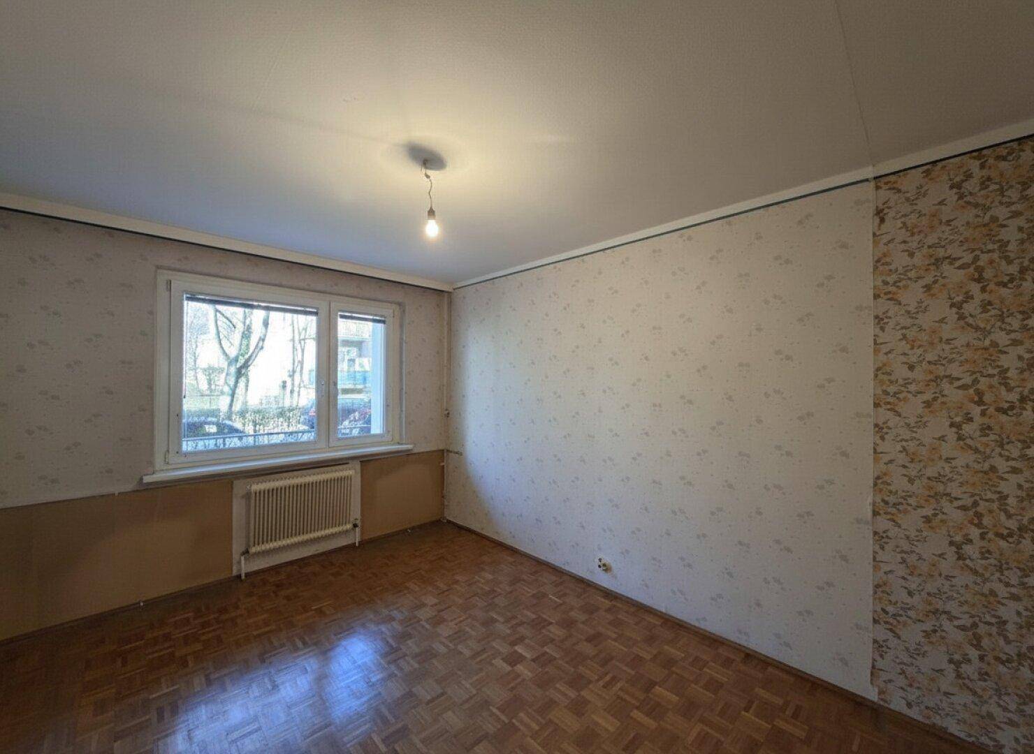 Leerer Raum mit älterer Tapete und Parkettboden, bereit für eine Renovierung.