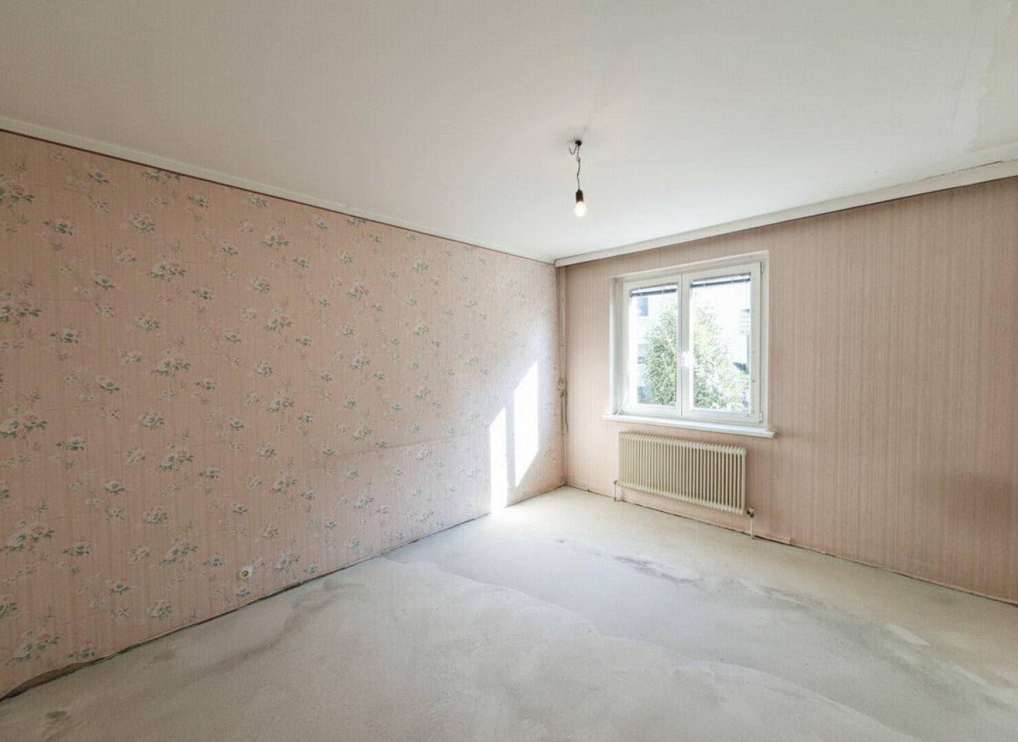 Leerer Raum mit abgenutzter Tapete und Betonboden, der eine umfassende Renovierung benötigt.