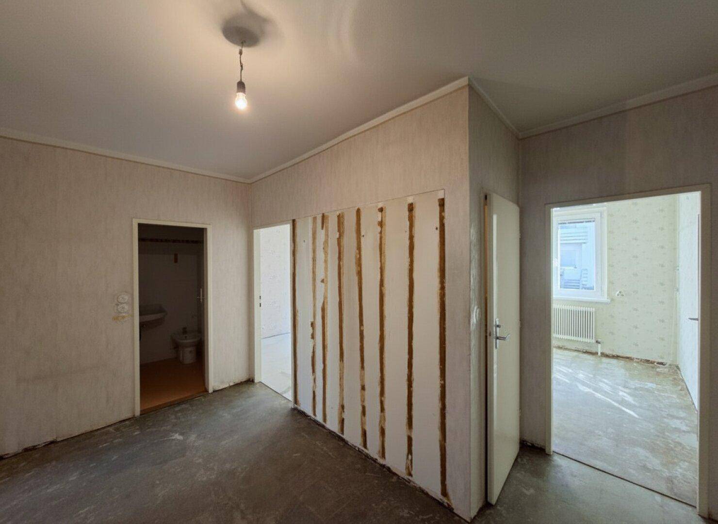 Flur mit mehreren Türen und Blick in ein Badezimmer, der auf eine Renovierung wartet.