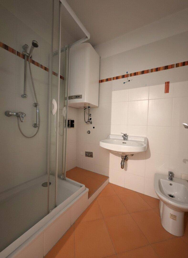 Badezimmer mit Duschkabine, Waschbecken, Bidet und einem Warmwasserboiler.
