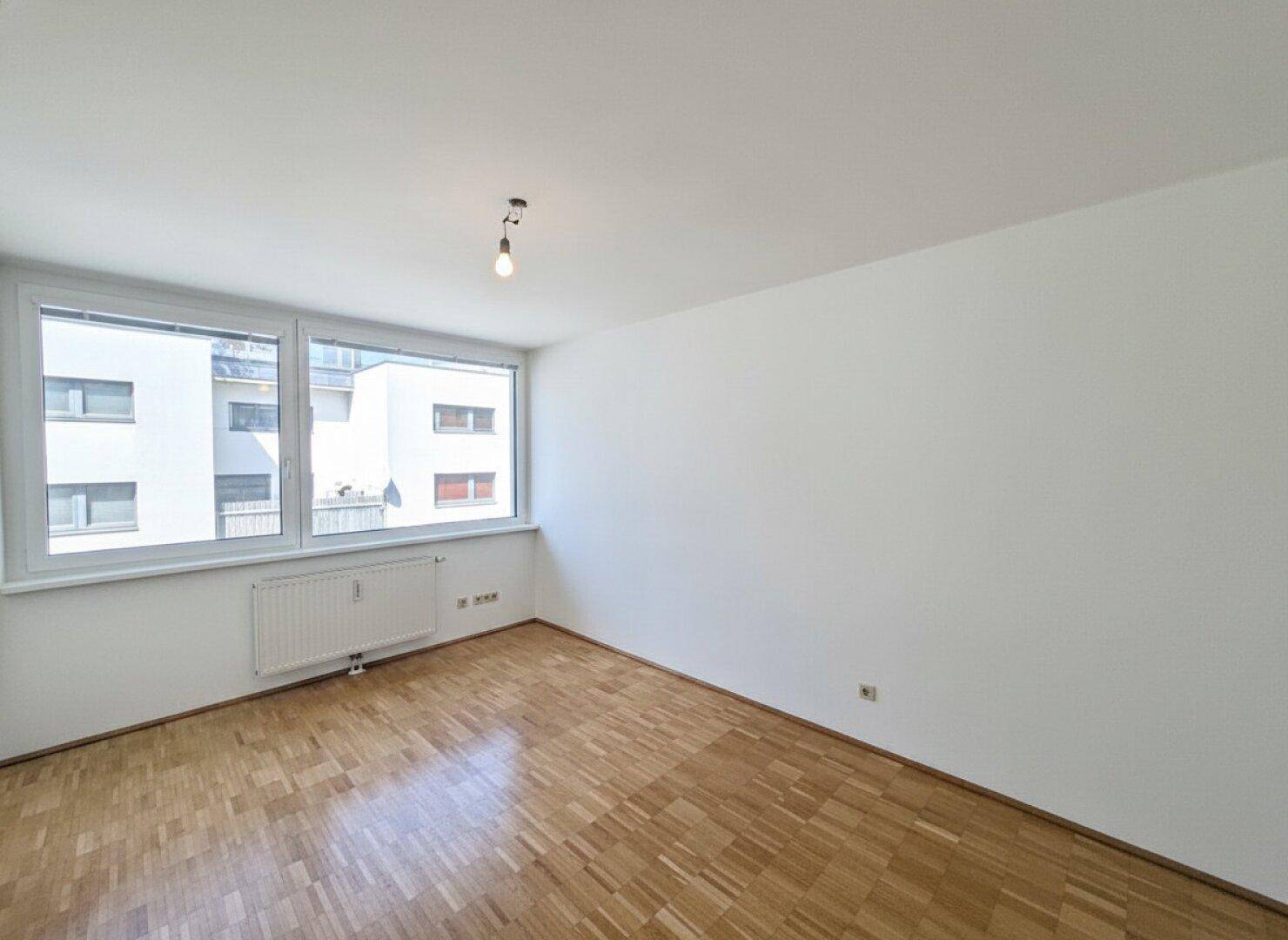 Helles Zimmer mit Parkettboden und großen Fenstern, die viel Tageslicht in den Raum lassen.