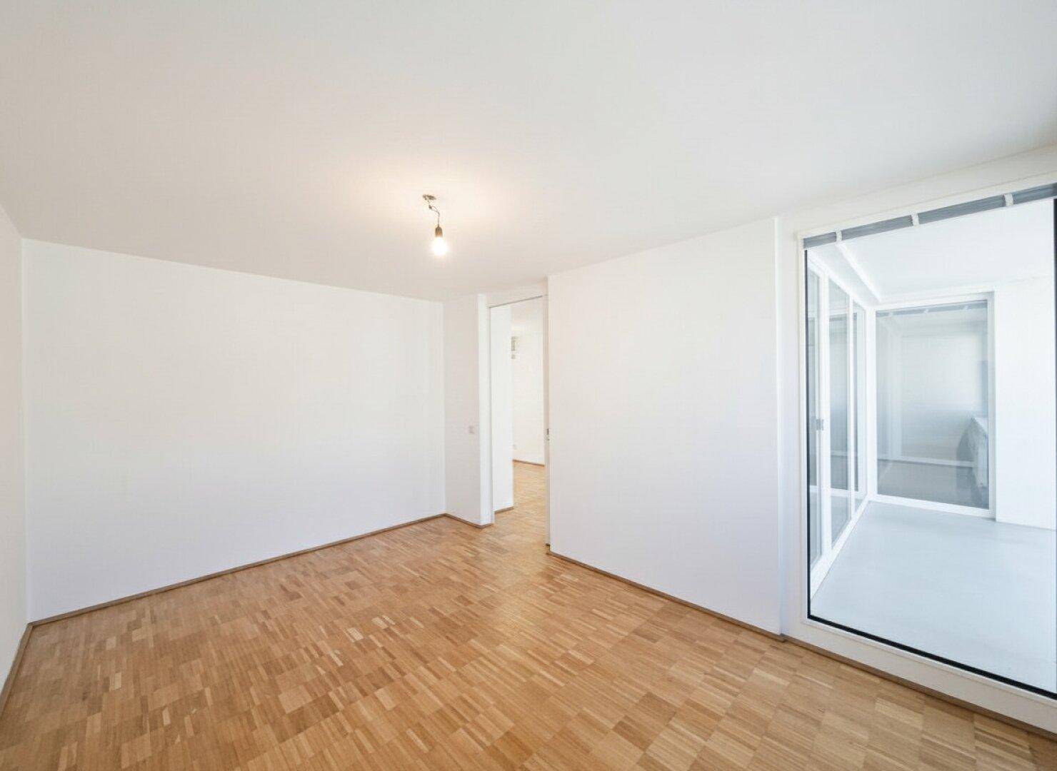Geräumiger Raum mit Parkettboden und direktem Zugang zu einer verglasten Loggia.