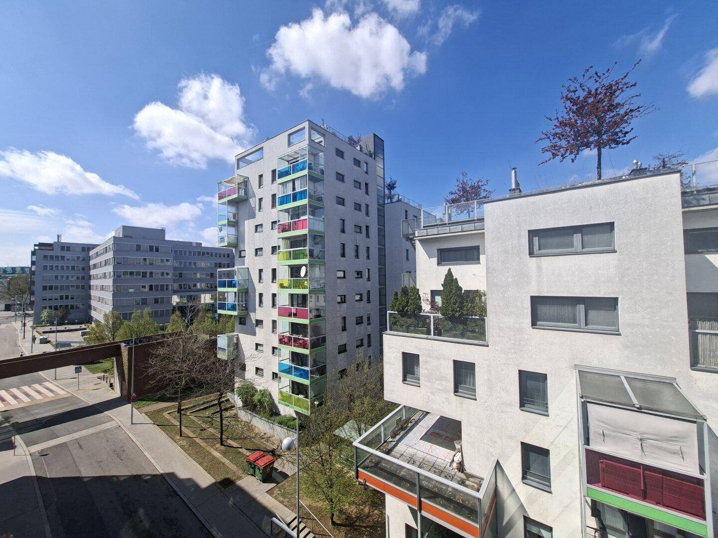 Moderne Wohngebäude mit farbigen Balkonen unter blauem Himmel in einer städtischen Umgebung.