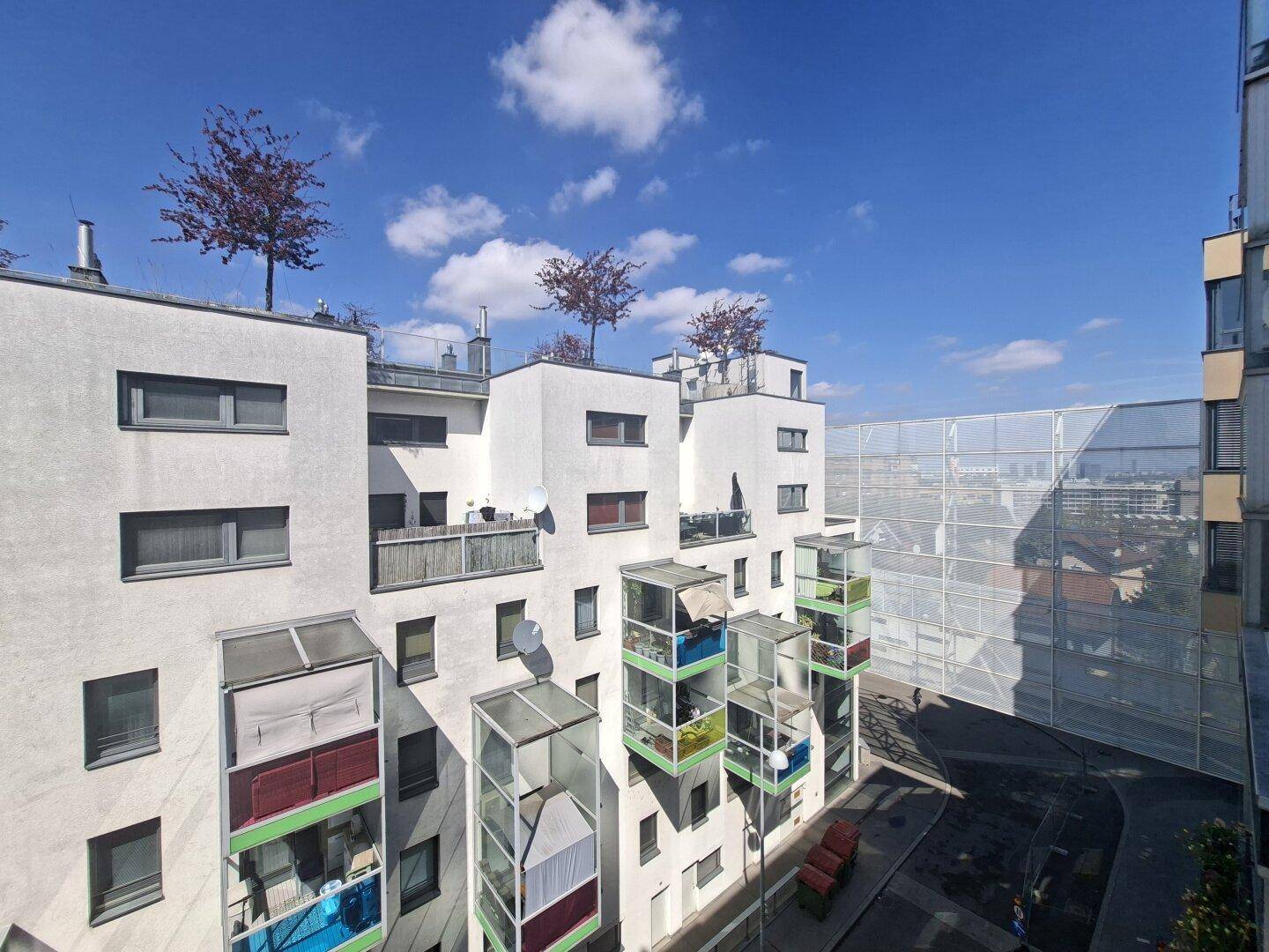 Ansicht der modernen Wohnanlage mit verglasten Balkonen und begrünten Dächern unter blauem Himmel.