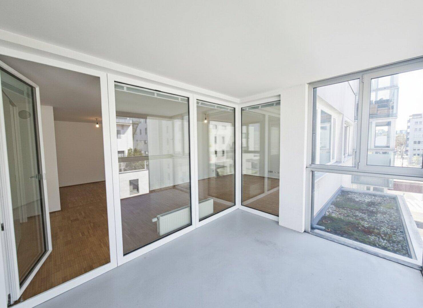 Verglaste Loggia mit Blick in den hellen Wohnbereich und auf die umliegenden Gebäude.