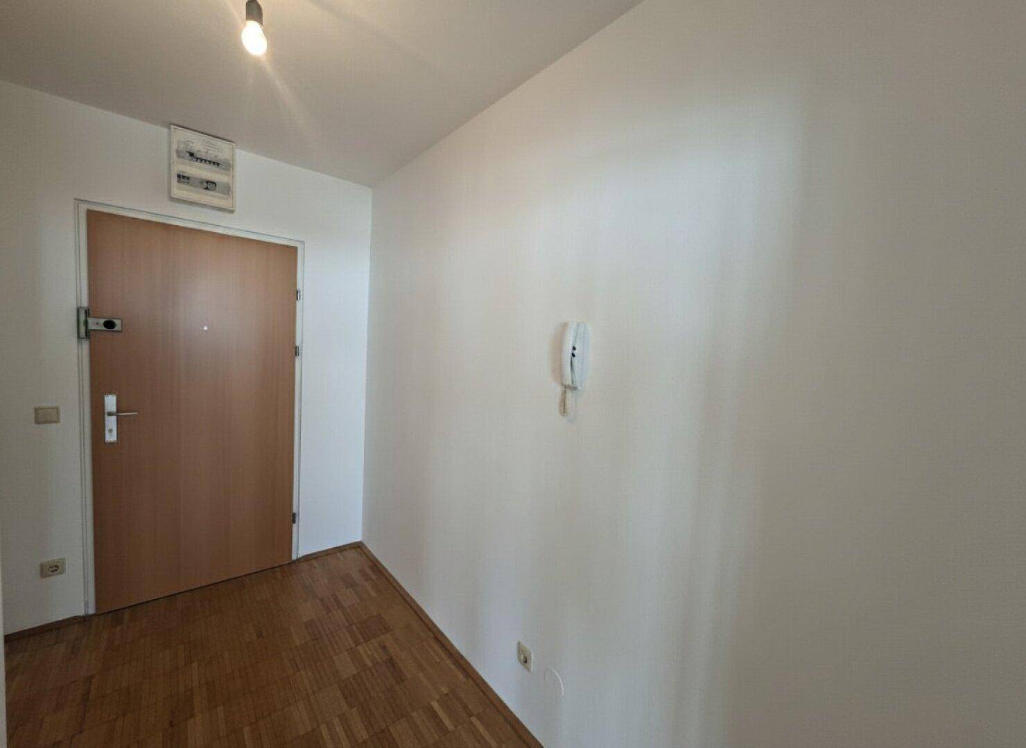 Eingangsbereich mit Holztür und Gegensprechanlage, der zu den Wohnräumen führt.