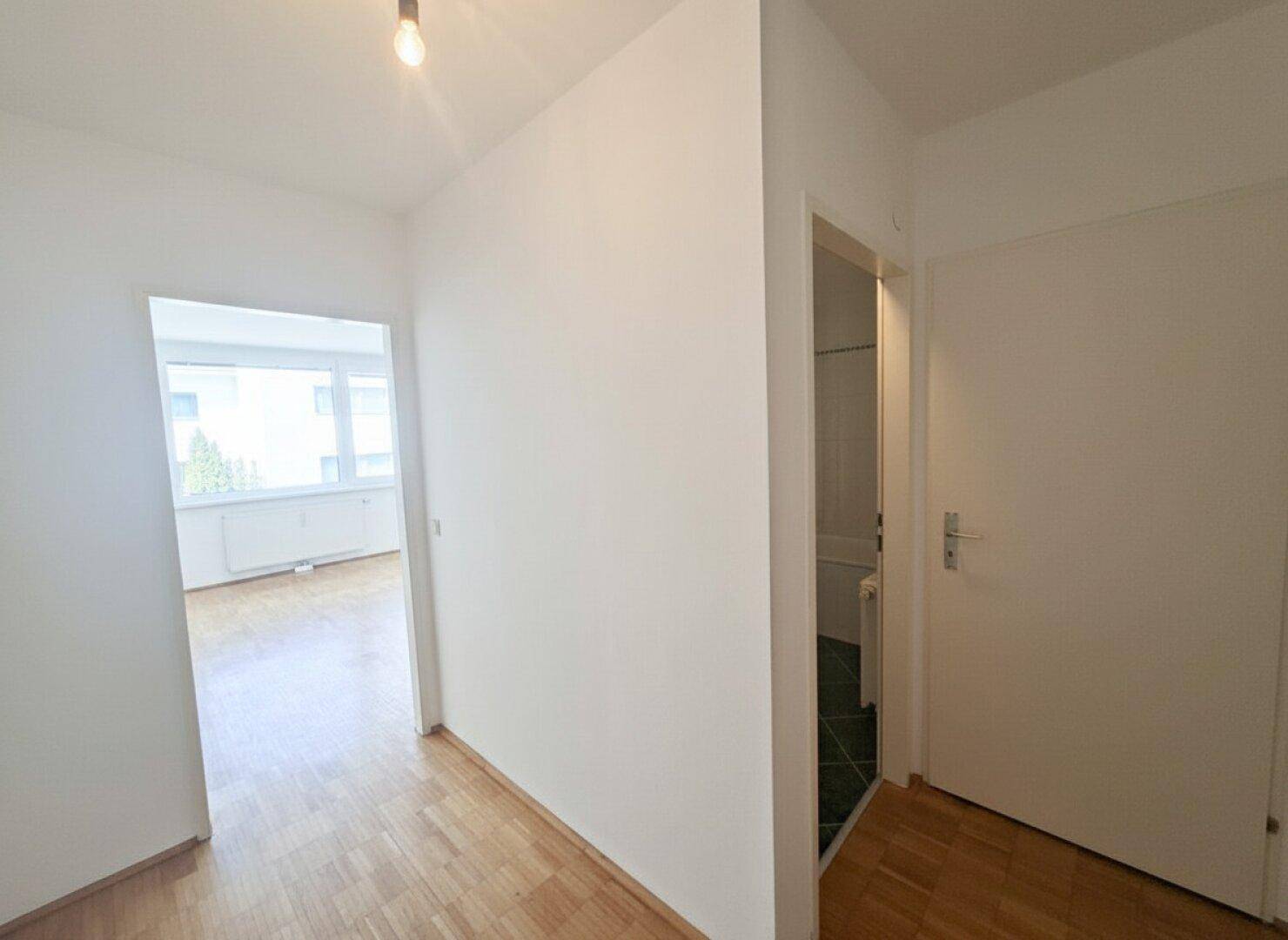 Heller Flur mit Parkettboden und Zugang zu einem Badezimmer sowie weiteren Zimmern.